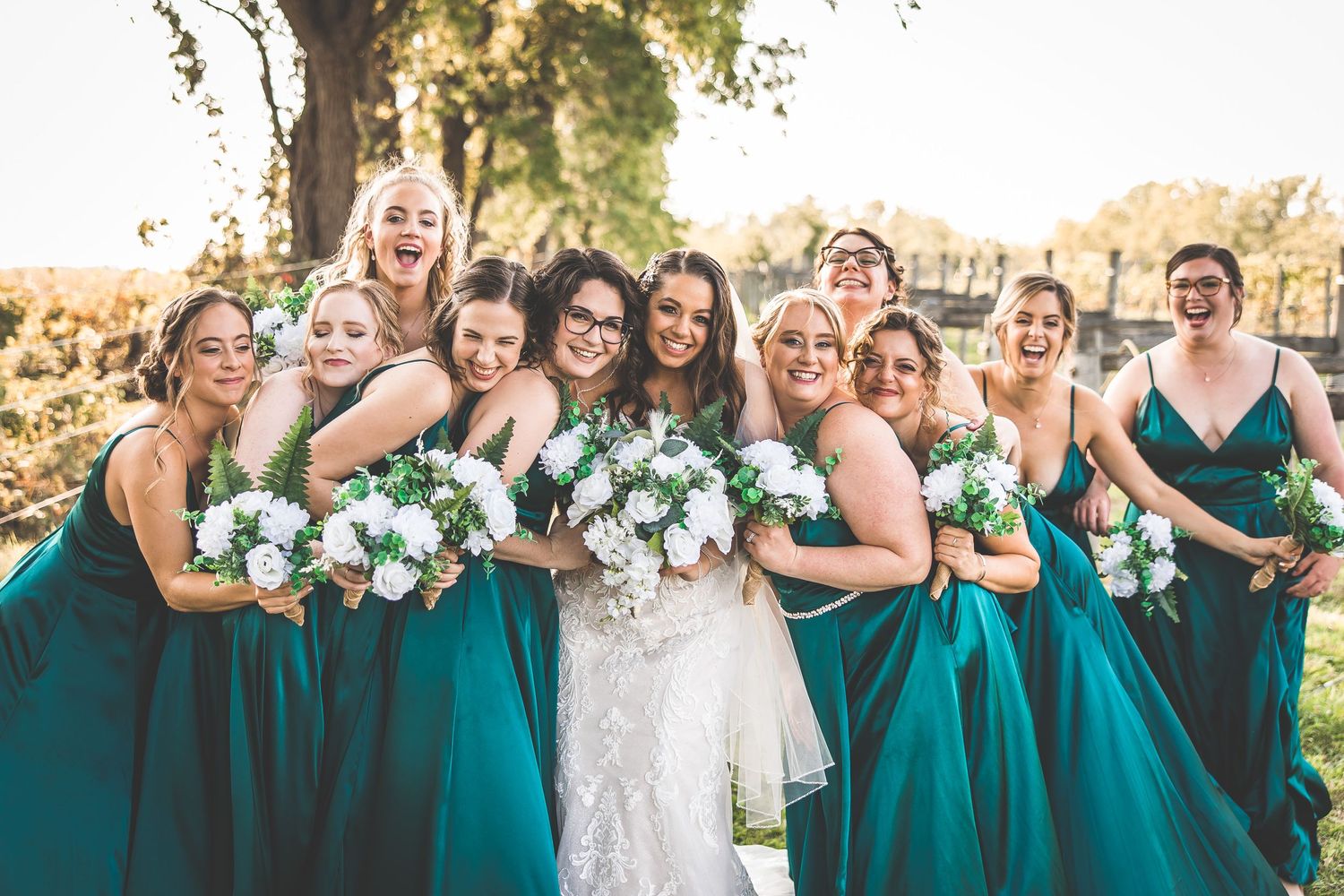 Wedding party members in teal dresses gather for group photos outdoors at sunset.