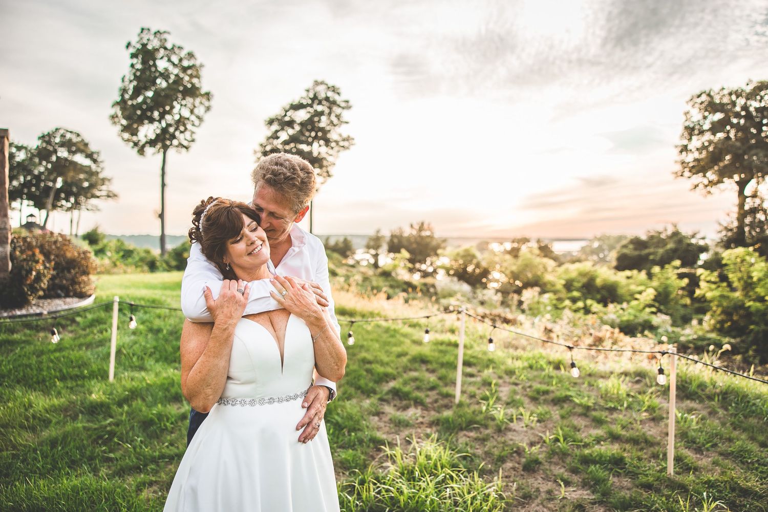 A couple shares a romantic embrace in a scenic vineyard at sunset.