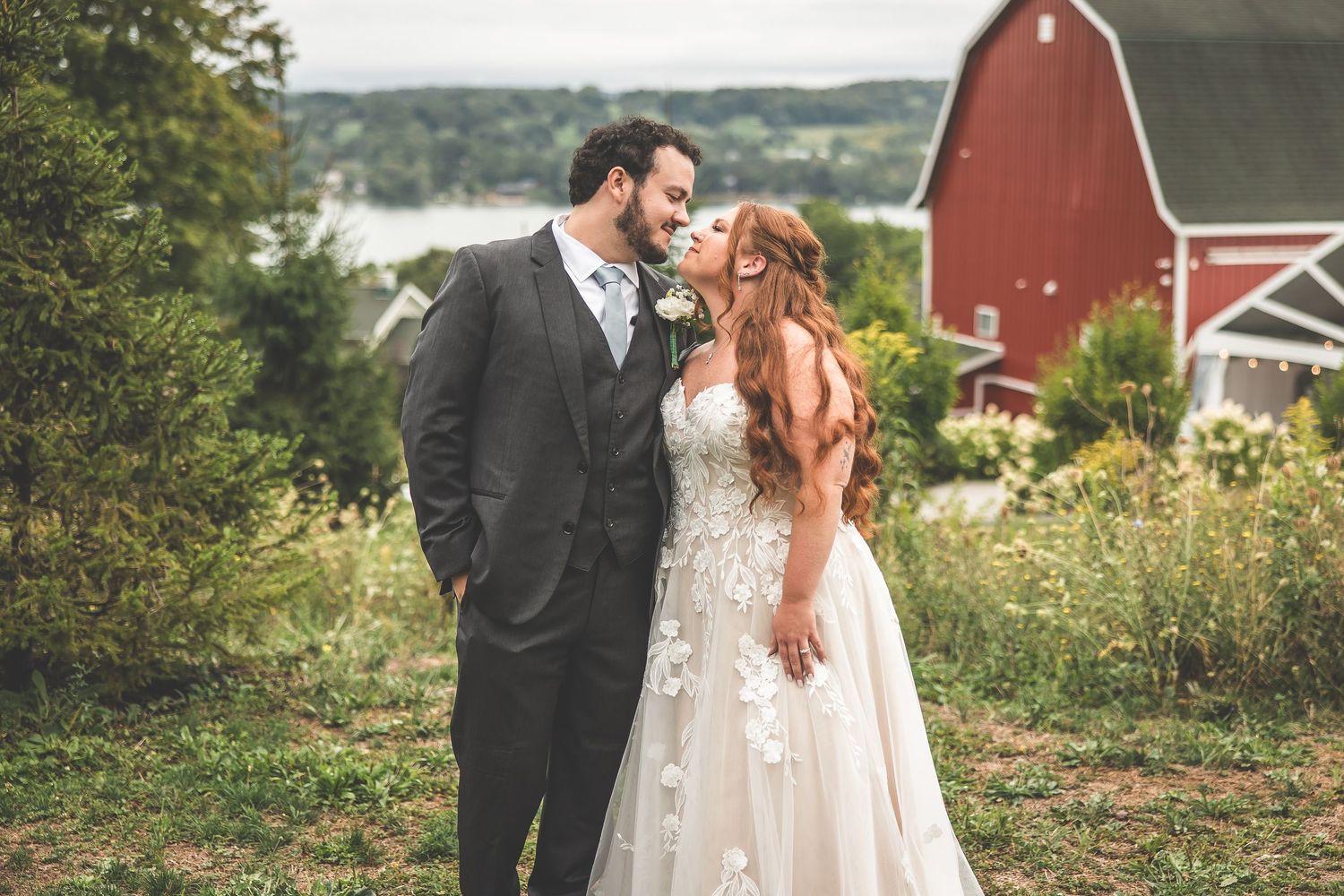 Wedding couple poses in front of a rustic red barn in a countryside setting.