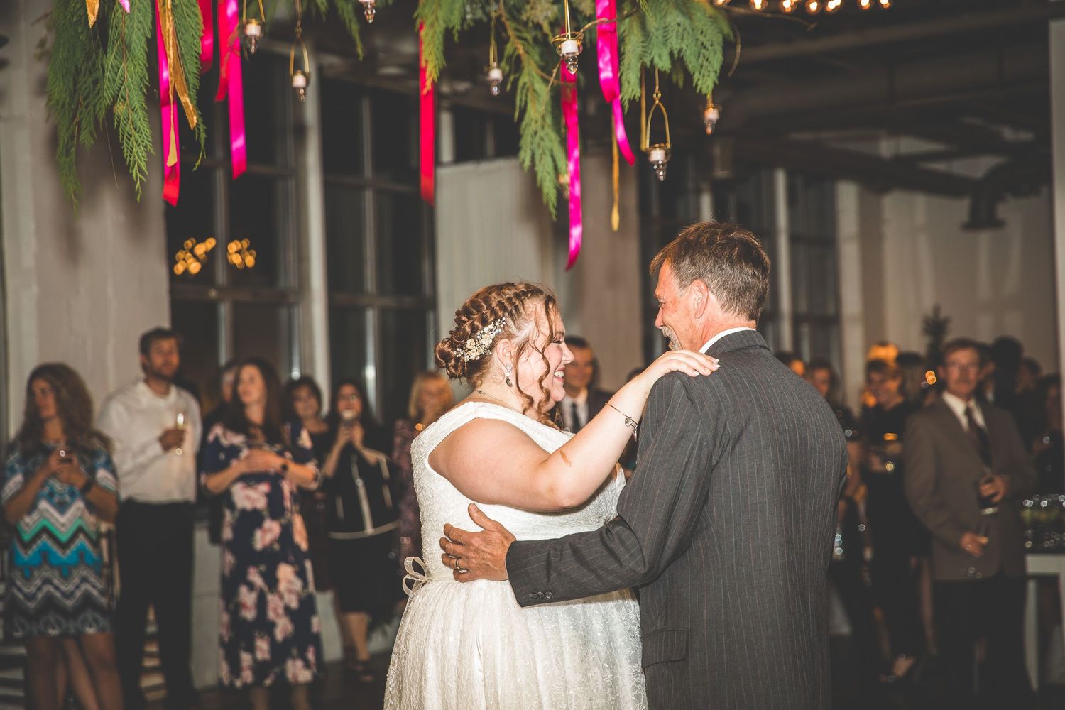 Wedding reception venue decorated with pink ribbons and greenery under warm lighting.