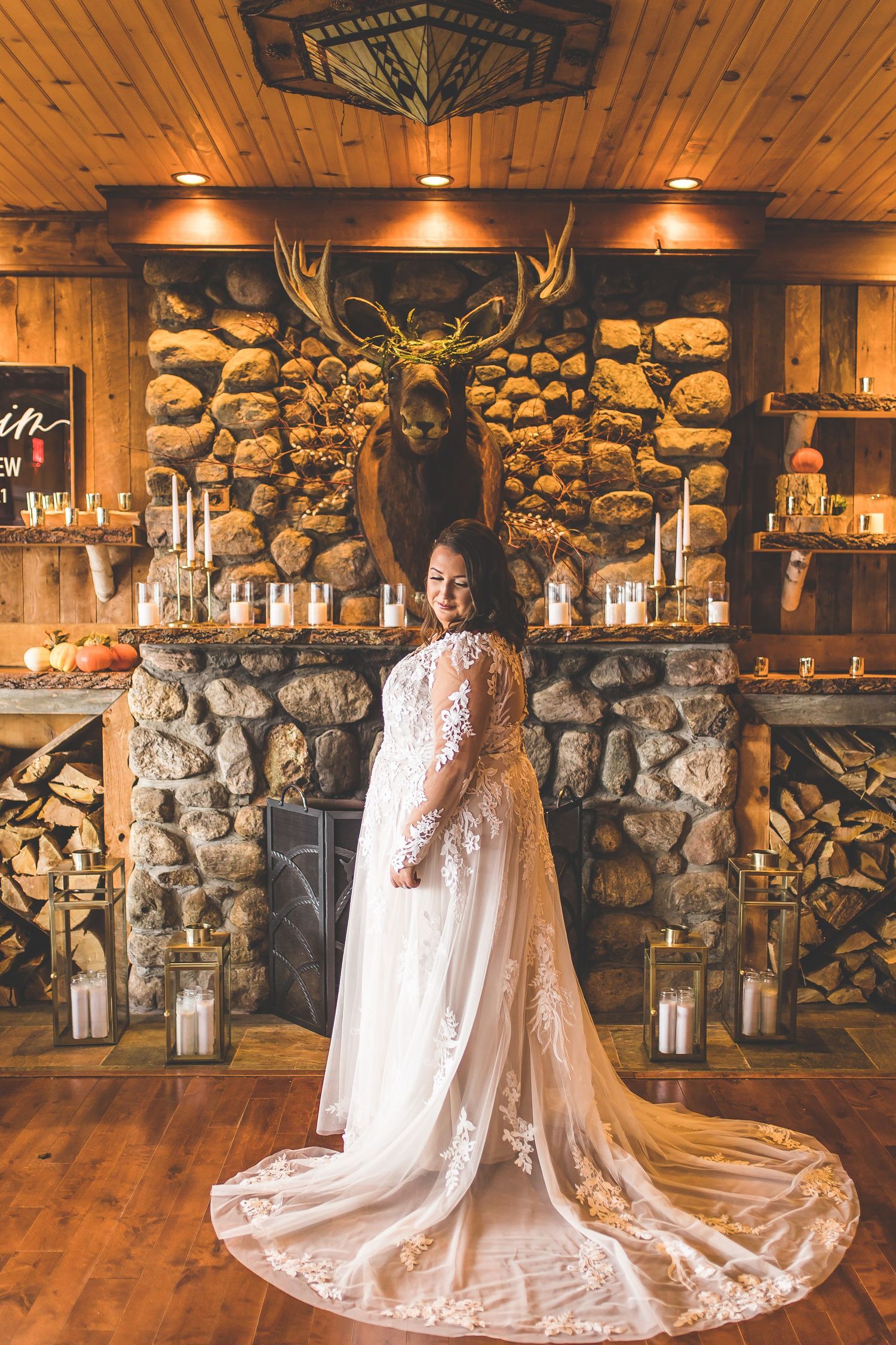 Bride in flowing lace gown photographed against stone wall with lantern decorations.