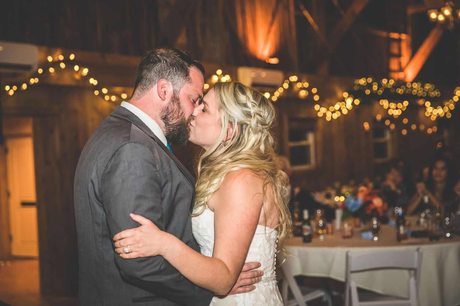 Wedding couple shares romantic dance moments in a rustic barn venue decorated with twinkling lights.