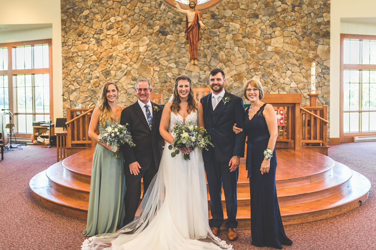 Wedding party lined up for formal photos in a church with stone walls and wooden altar.