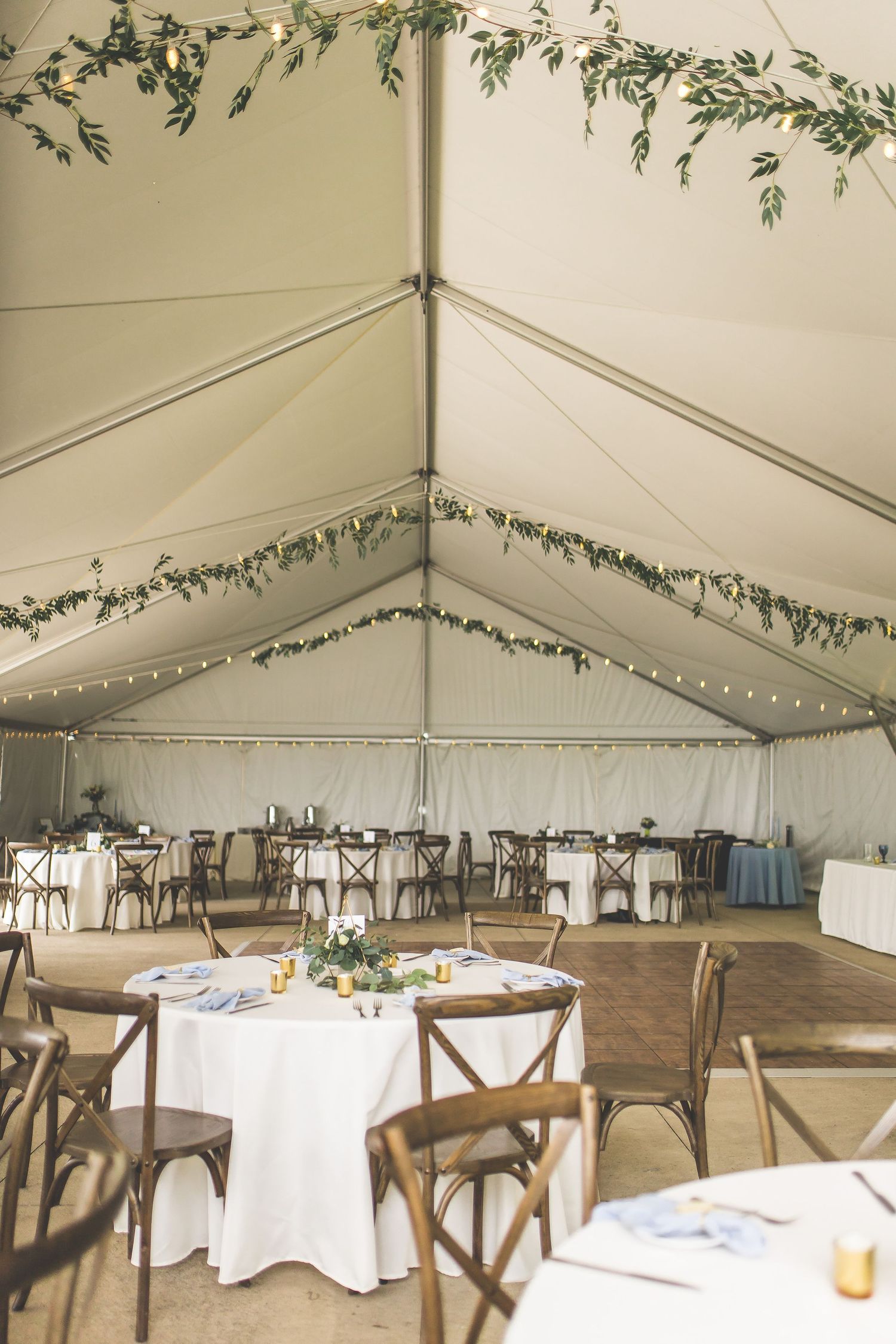 Elegant wedding reception tent interior with white linens and greenery garland decorations.