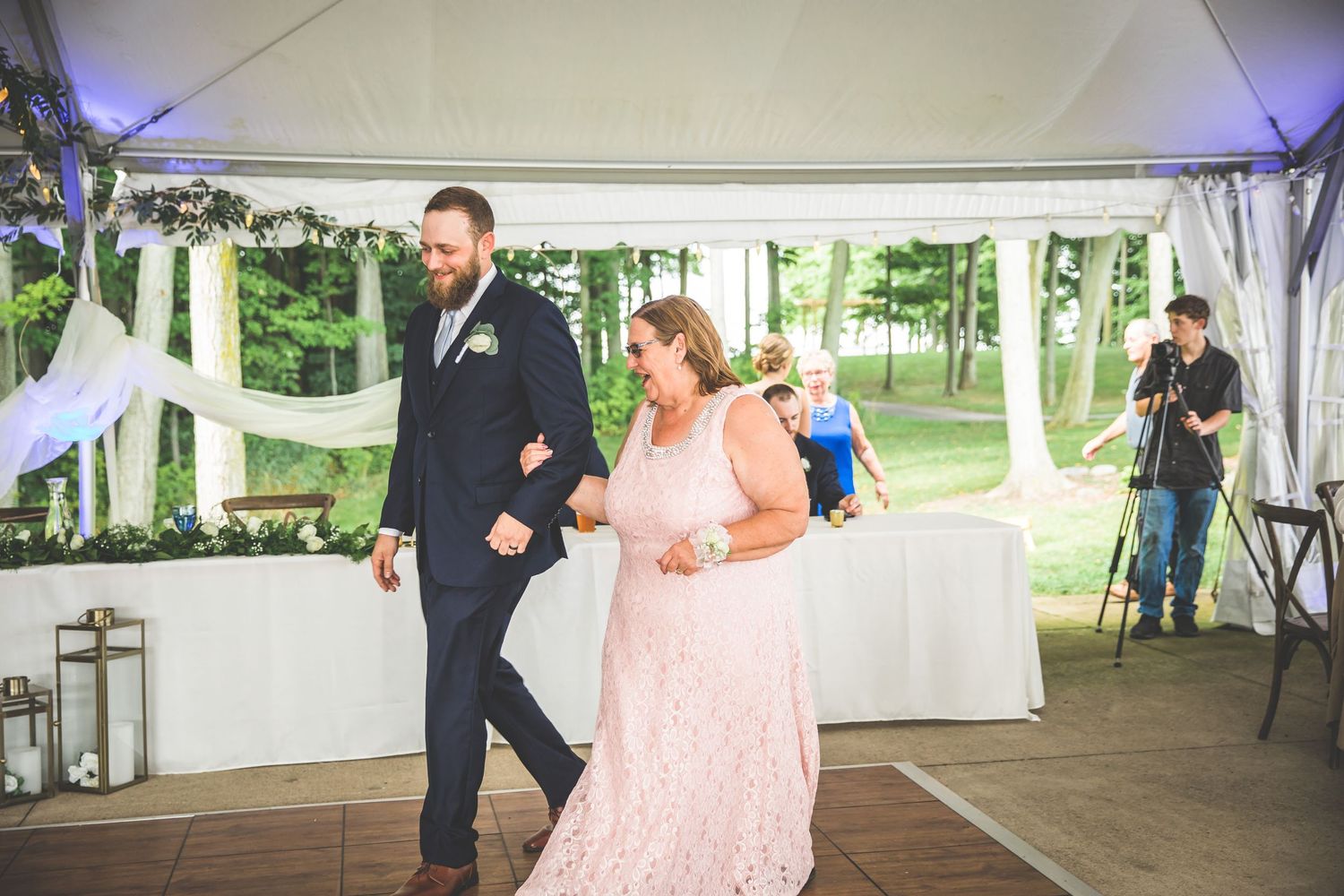 Wedding celebration in an outdoor tent venue decorated with string lights and floral arrangements.