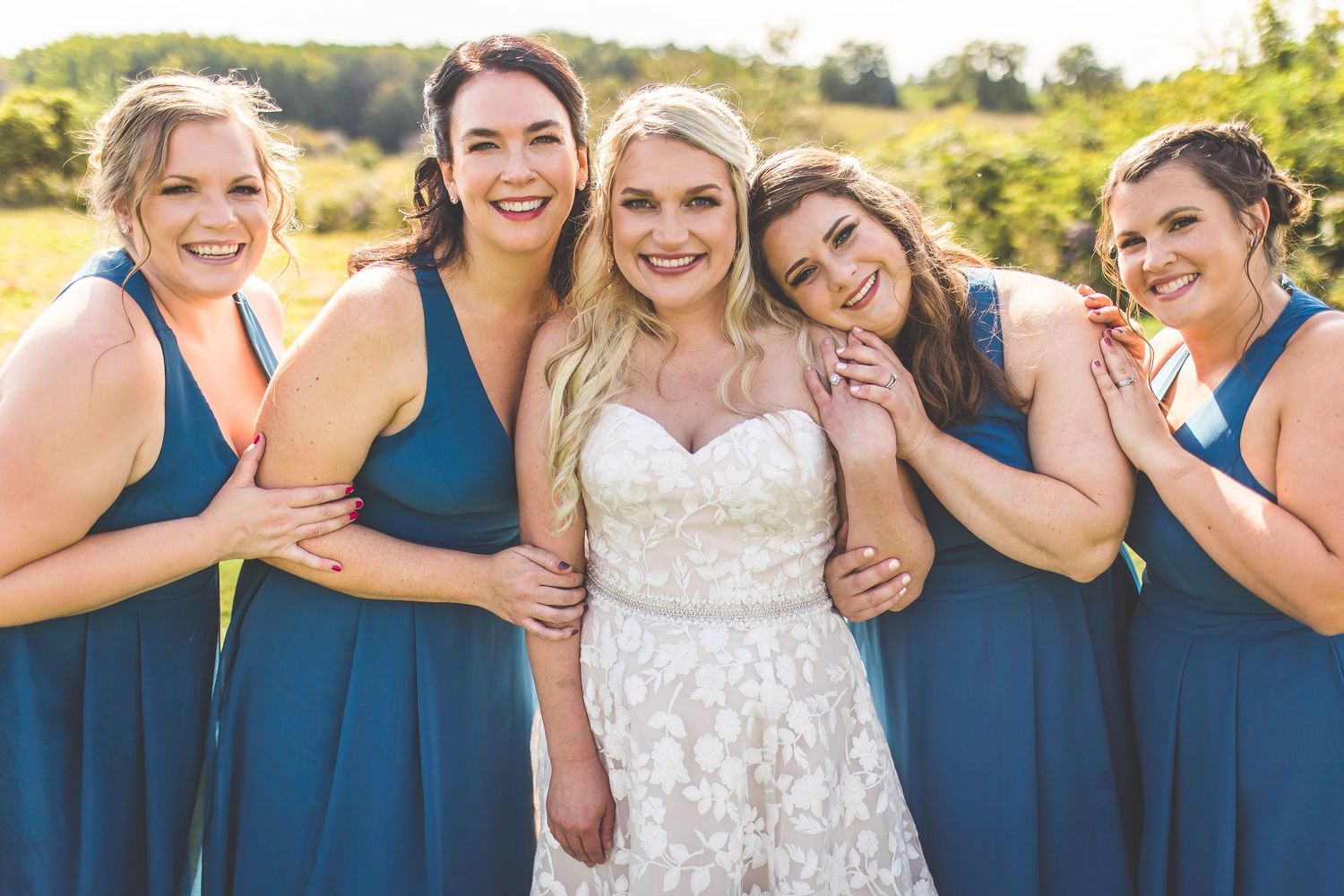 Candid laughing moment between bridesmaids in navy and bride in white lace.