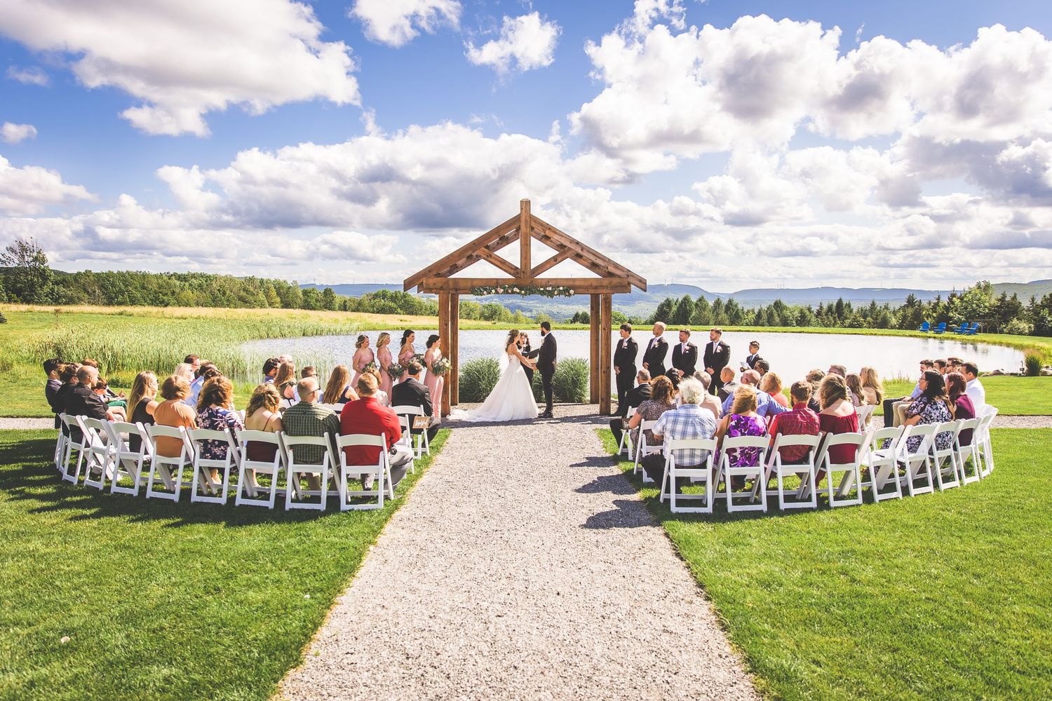 A scenic outdoor wedding ceremony under a wooden pavilion with white chairs and lake views.