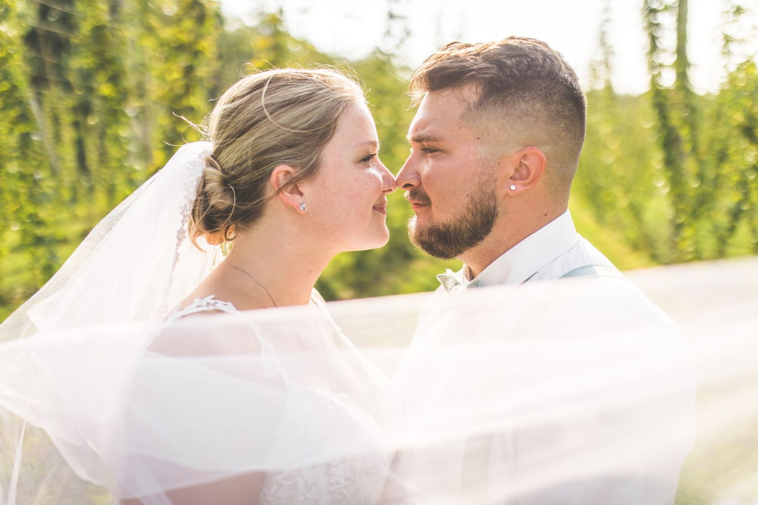 Romantic outdoor wedding portraits with a flowing veil catching the sunlight in a natural setting.