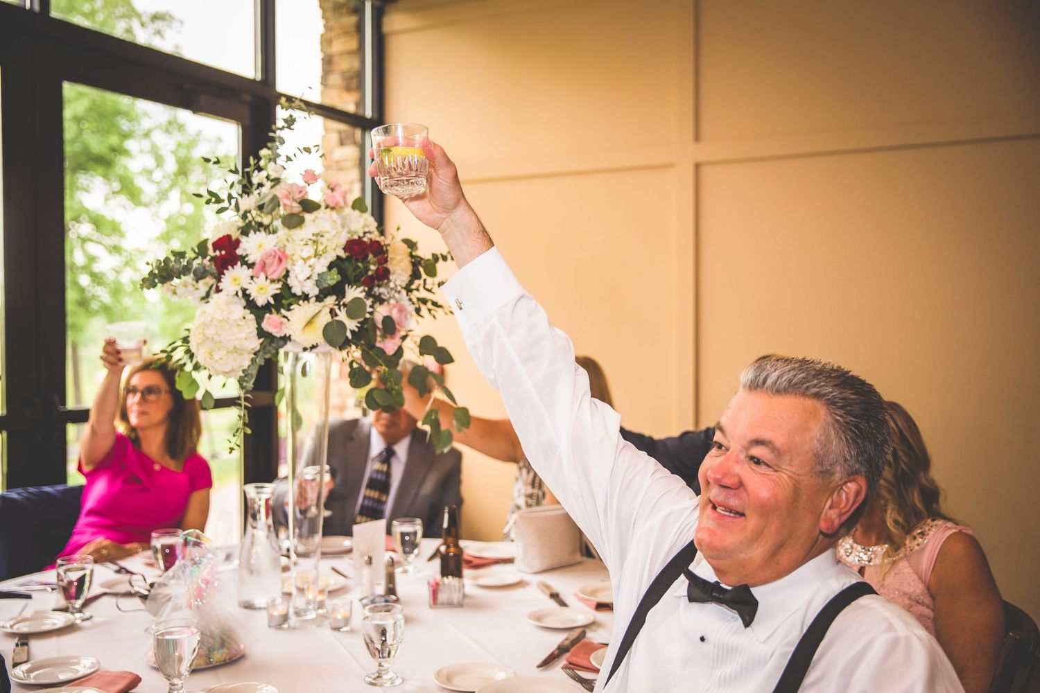A guest raises a glass during an elegant wedding reception with floral centerpieces.