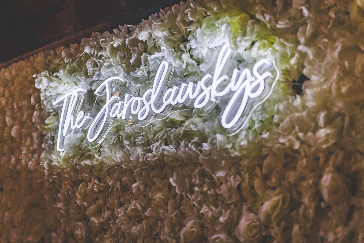 Illuminated neon cursive sign reading 'The Jaroslavskys' mounted on a textured wall.