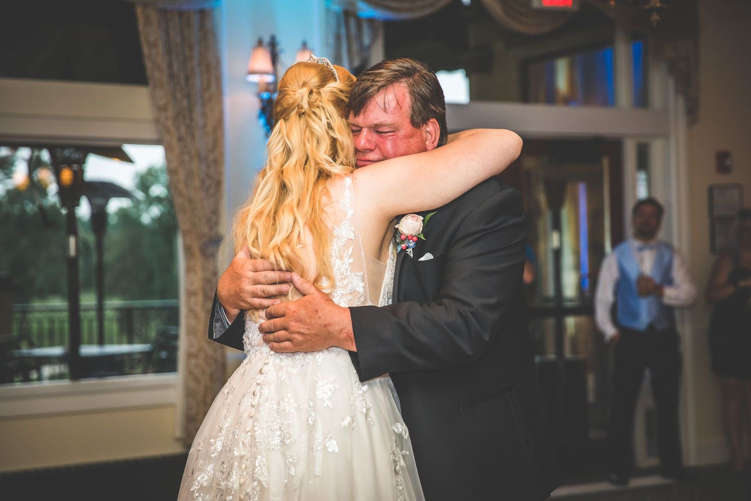Wedding couple shares an intimate dance moment on a patterned ballroom floor under elegant chandeliers.