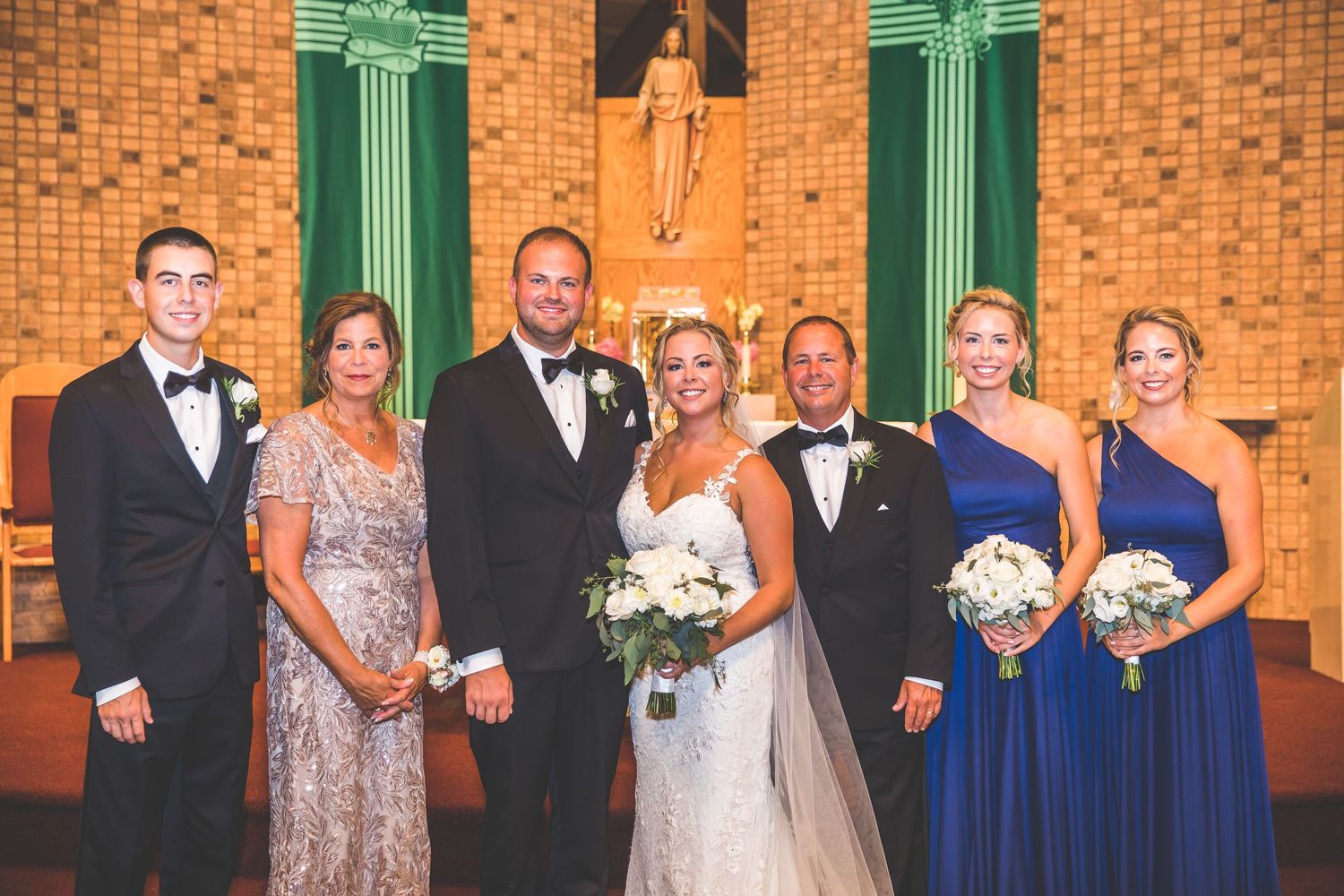 Formal wedding party group photos with bridesmaids in blue dresses against brick church wall.