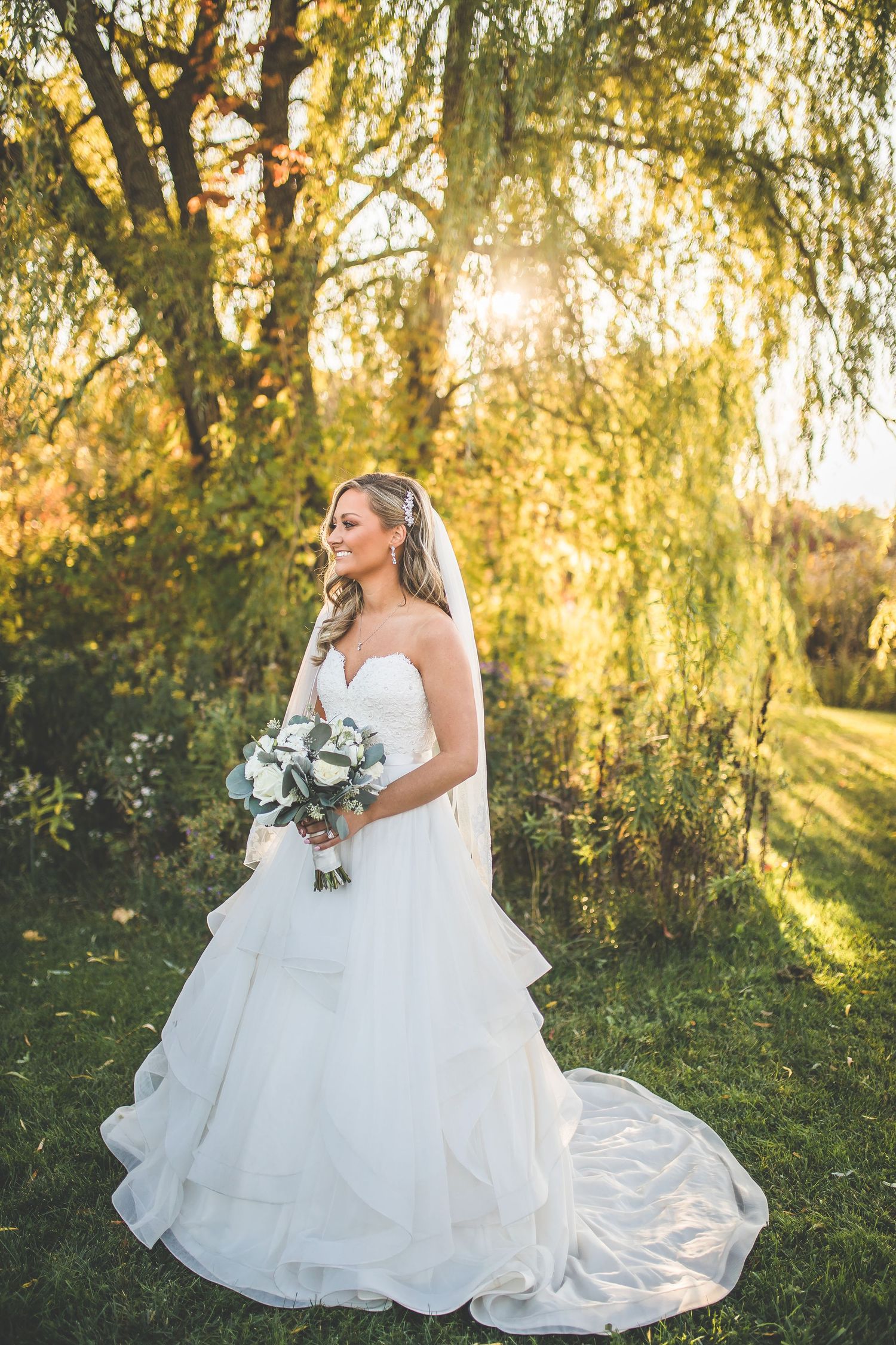Bridal portraits in a white gown against golden sunlit willow trees.