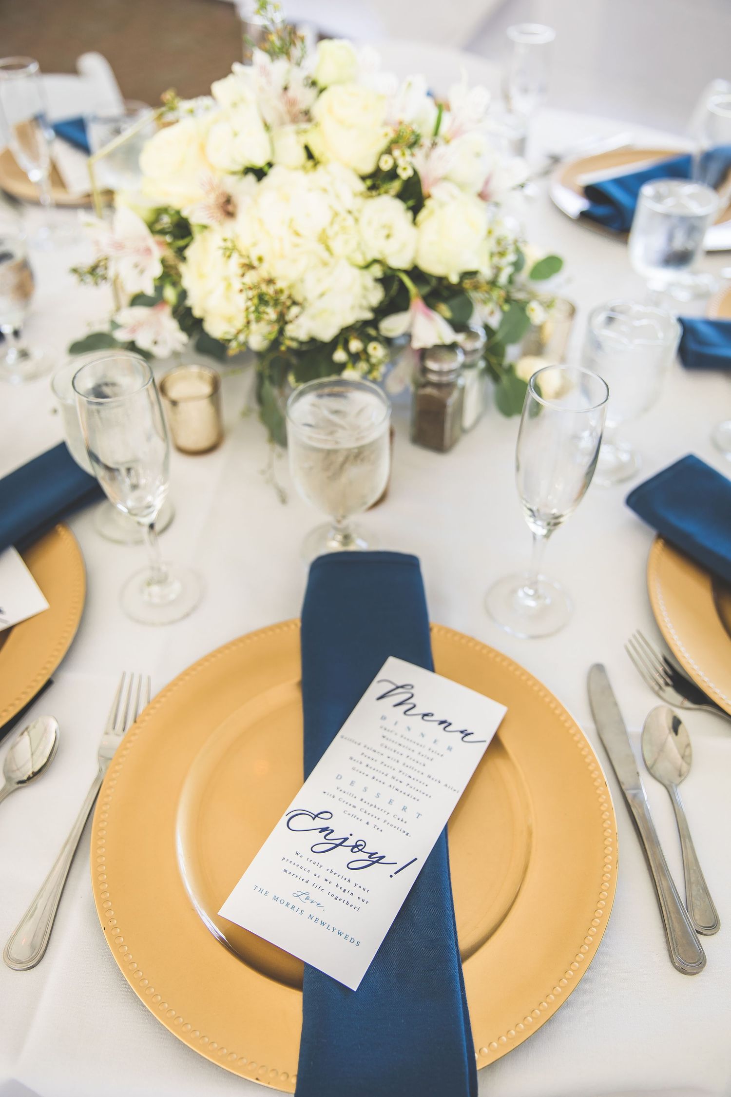 Elegant place settings with gold chargers, navy napkins and white floral centerpieces.
