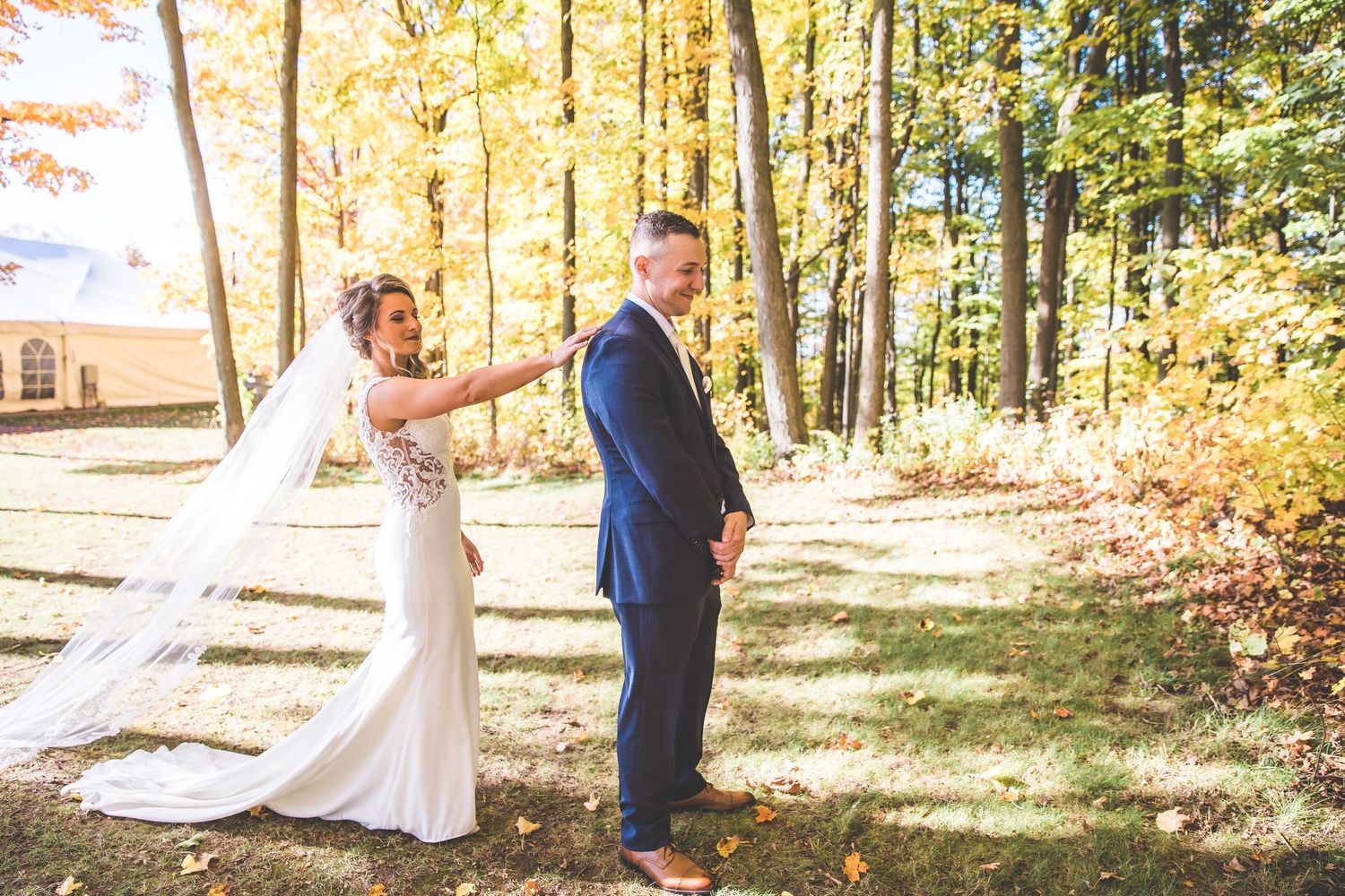 Wedding couple poses in autumn forest with golden leaves and sunlight filtering through trees.