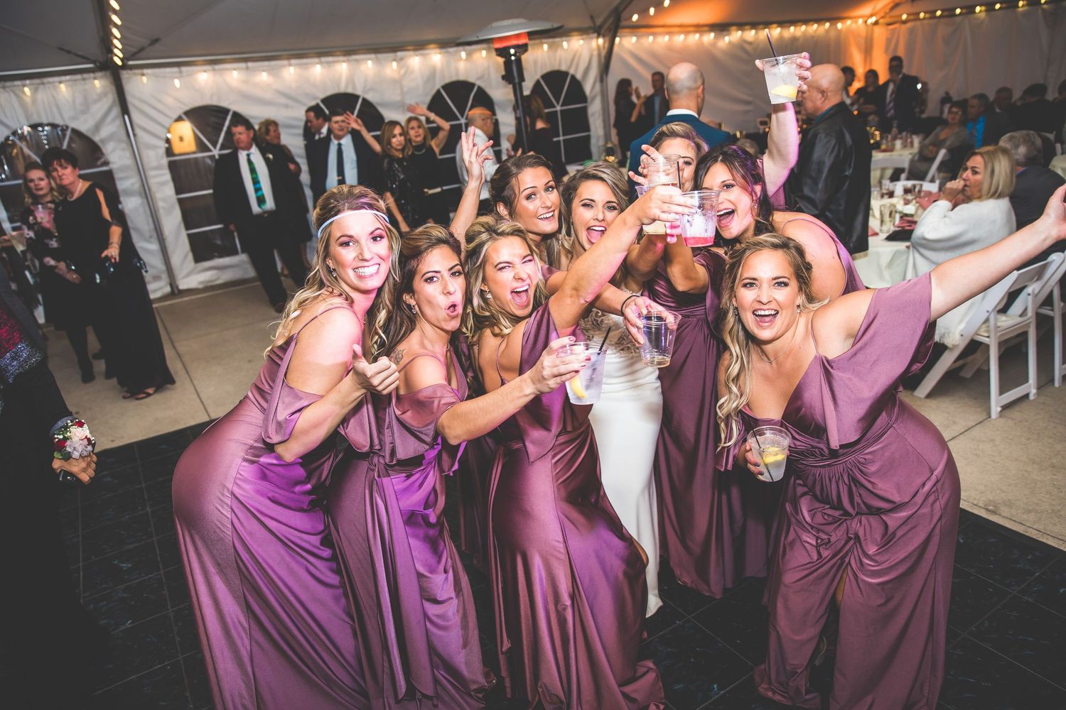 Bridesmaids in purple dresses celebrate together during a wedding reception.