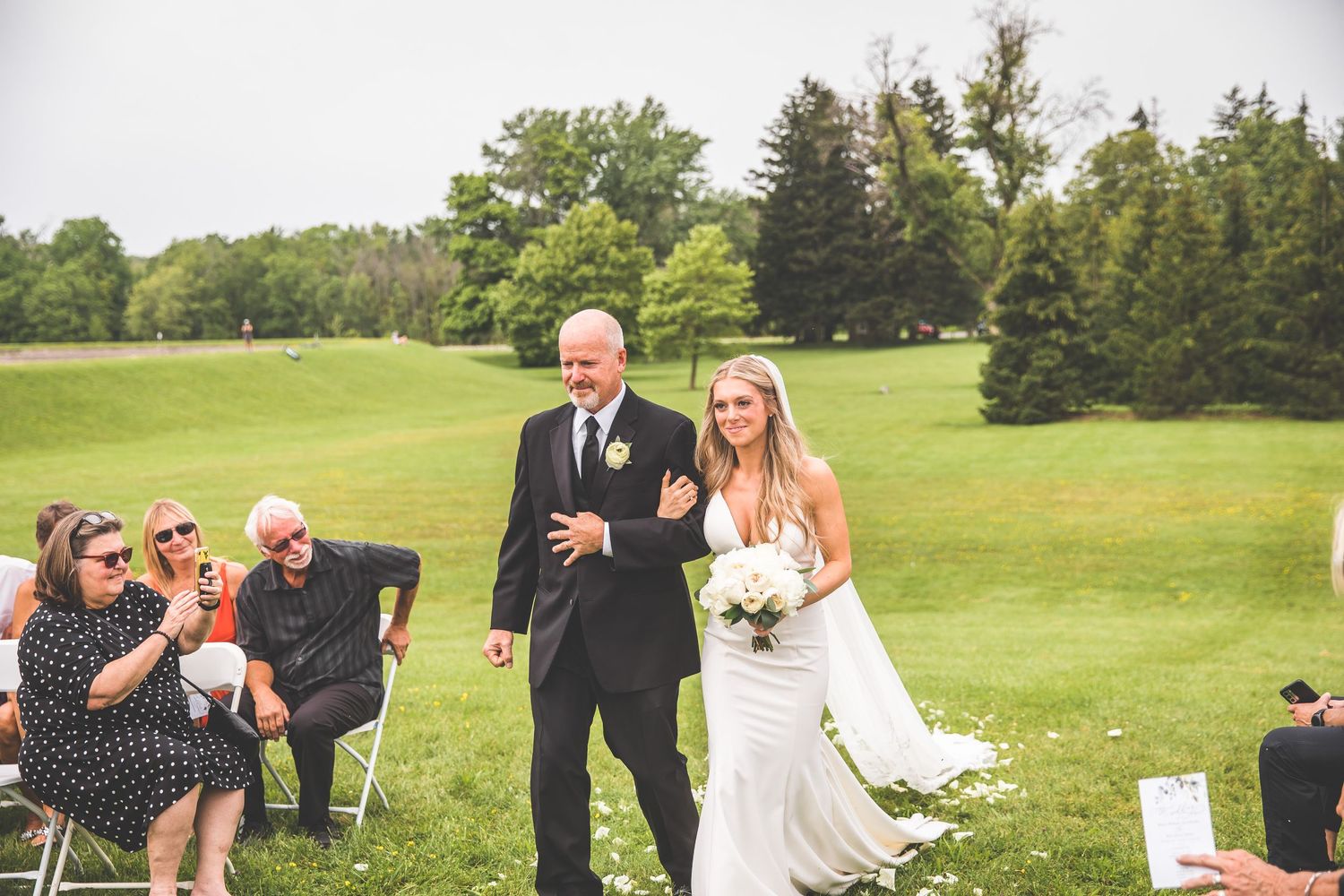 Wedding guests and party members gather on manicured lawn for outdoor celebration.