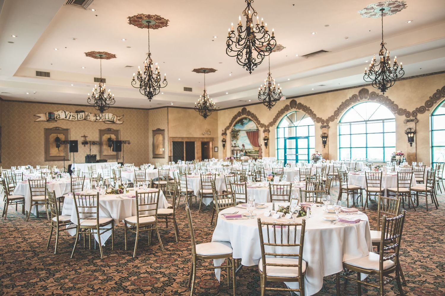 Elegant ballroom with crystal chandeliers set up for wedding reception with round tables and chiavari chairs.