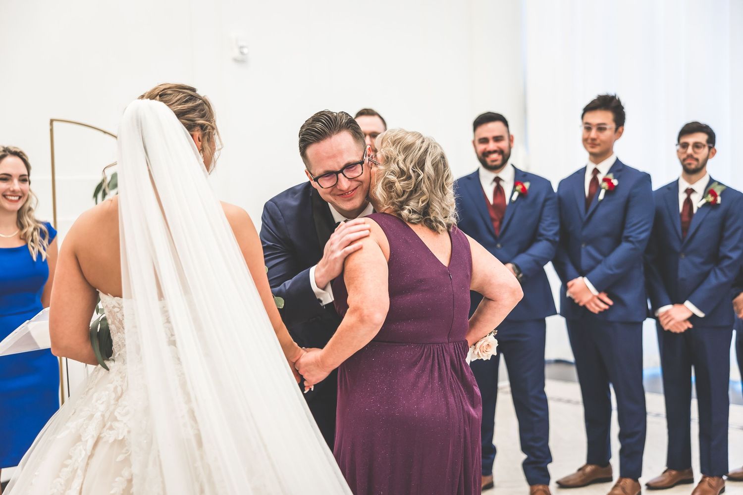 Wedding party lineup in a modern white venue with bridesmaids in burgundy dresses.