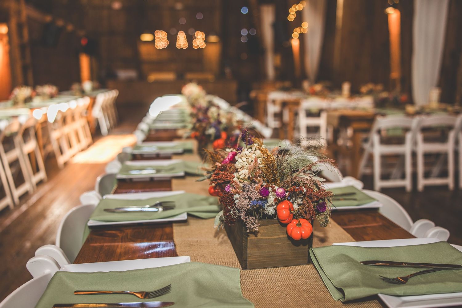 Rustic barn wedding reception tables set with sage green linens and floral centerpieces.