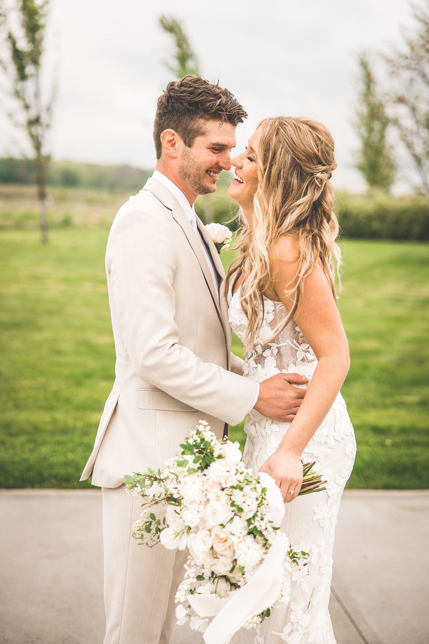 Intimate moment between newlyweds in beige suit and white dress on outdoor patio.