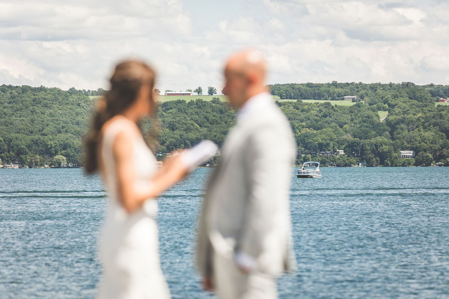 An intimate wedding moment captured in soft focus with a lake and hills in the background.
