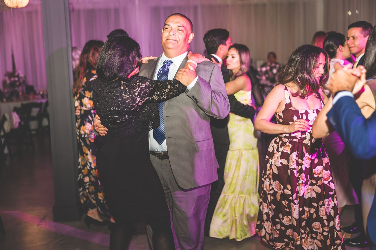 Wedding reception dance floor filled with guests dancing under purple mood lighting.