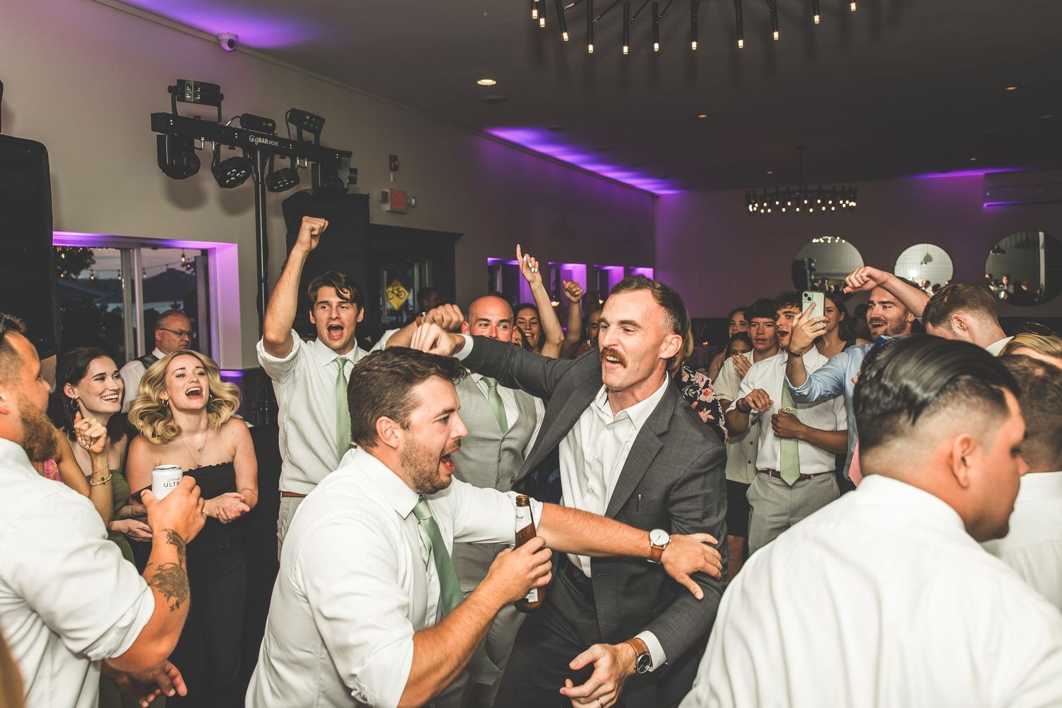 Reception dance floor filled with guests celebrating under purple ambient lighting.