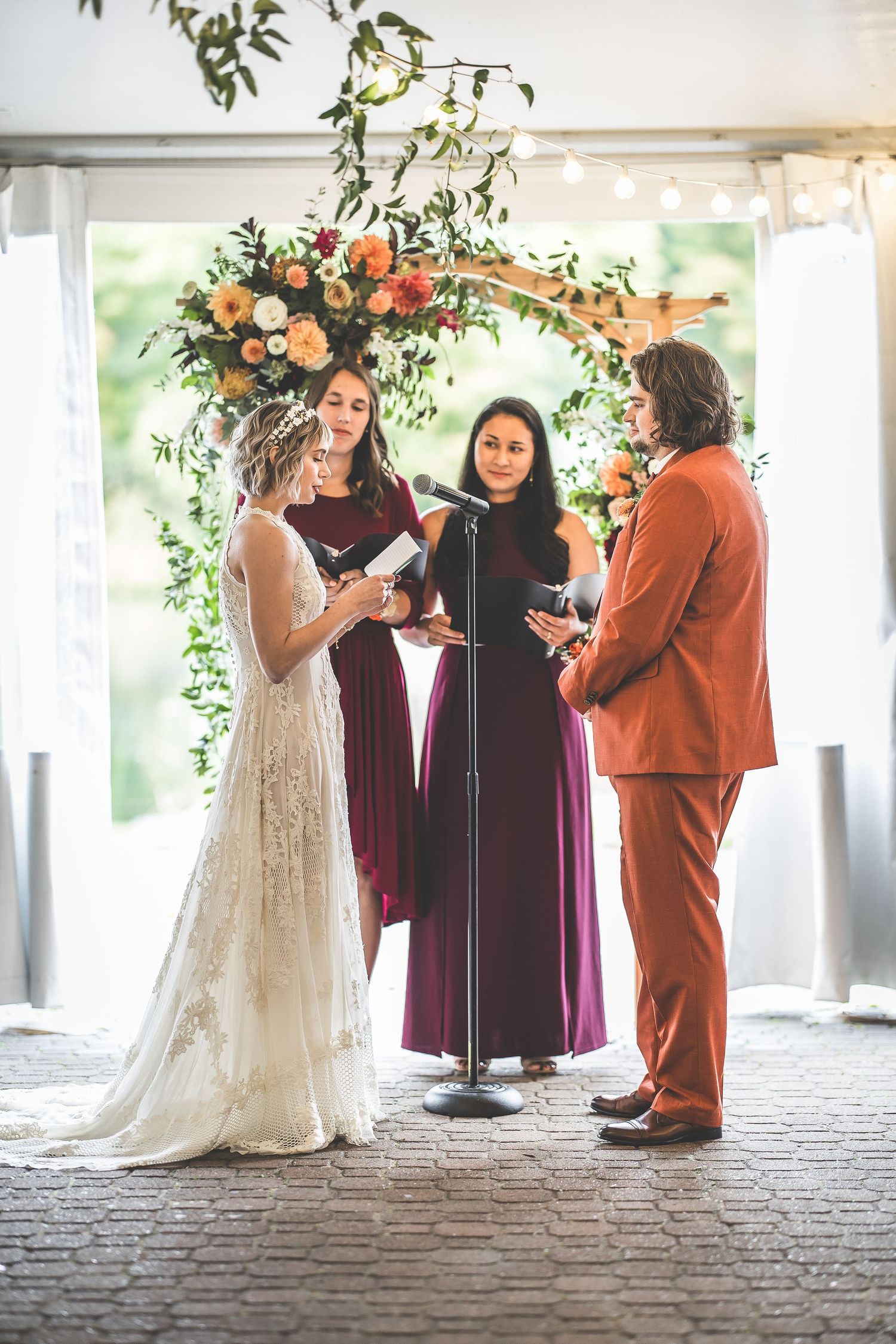 Wedding ceremony in progress with elegant floral arch and burgundy bridesmaids dresses.