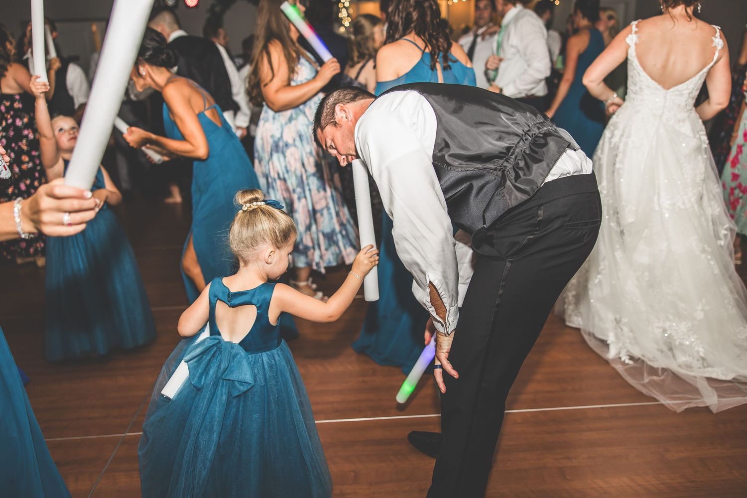 Wedding celebration on dance floor with bridesmaids in teal dresses and guests dancing.