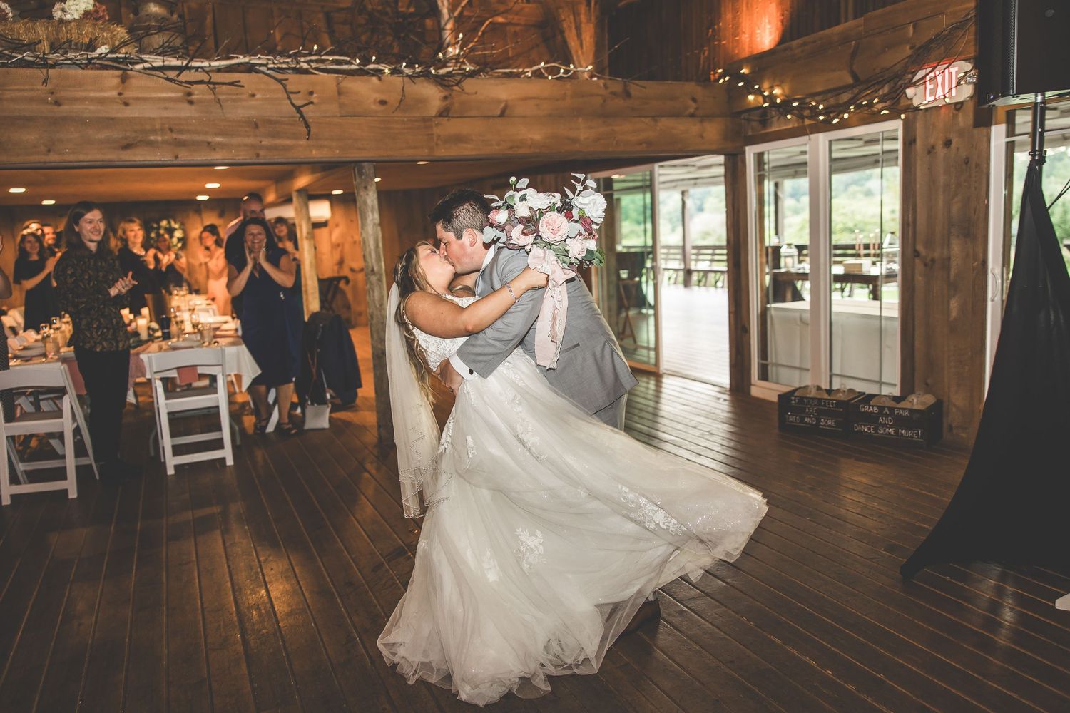 Couple performs romantic dance moves on wooden floor of elegantly lit barn wedding venue.