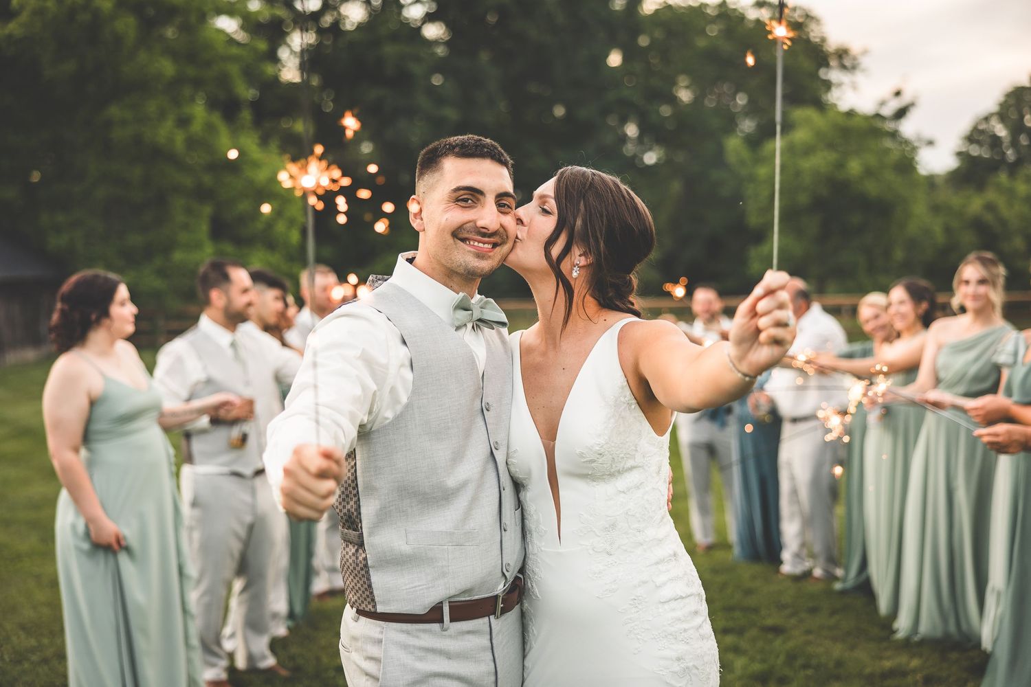 Wedding party celebrating with sparklers during outdoor evening reception.