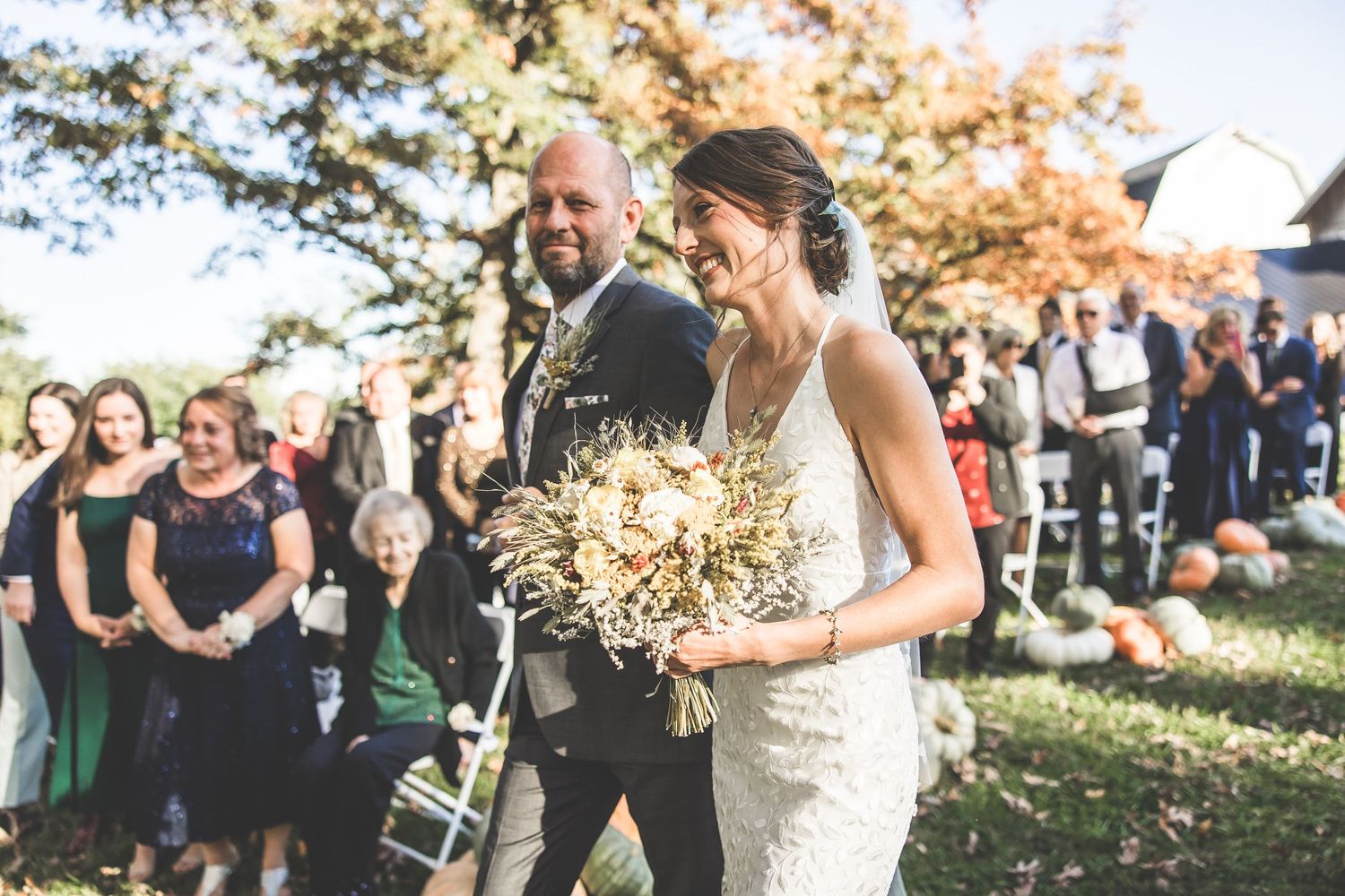 Wedding guests look on as the newlyweds walk past during an outdoor autumn ceremony.