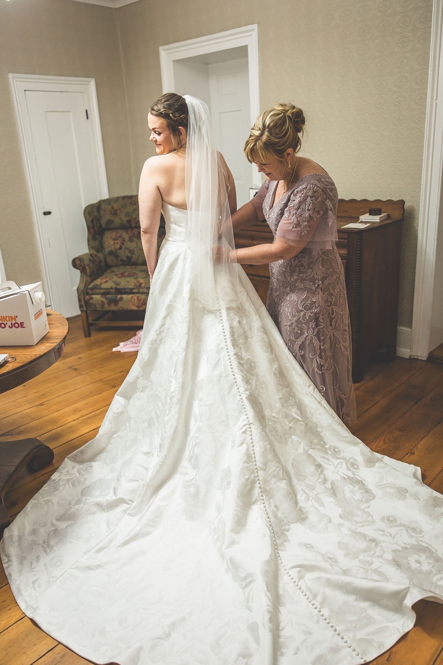 Detailed view of ornate wedding dress train with buttons and lace details on hardwood floor.