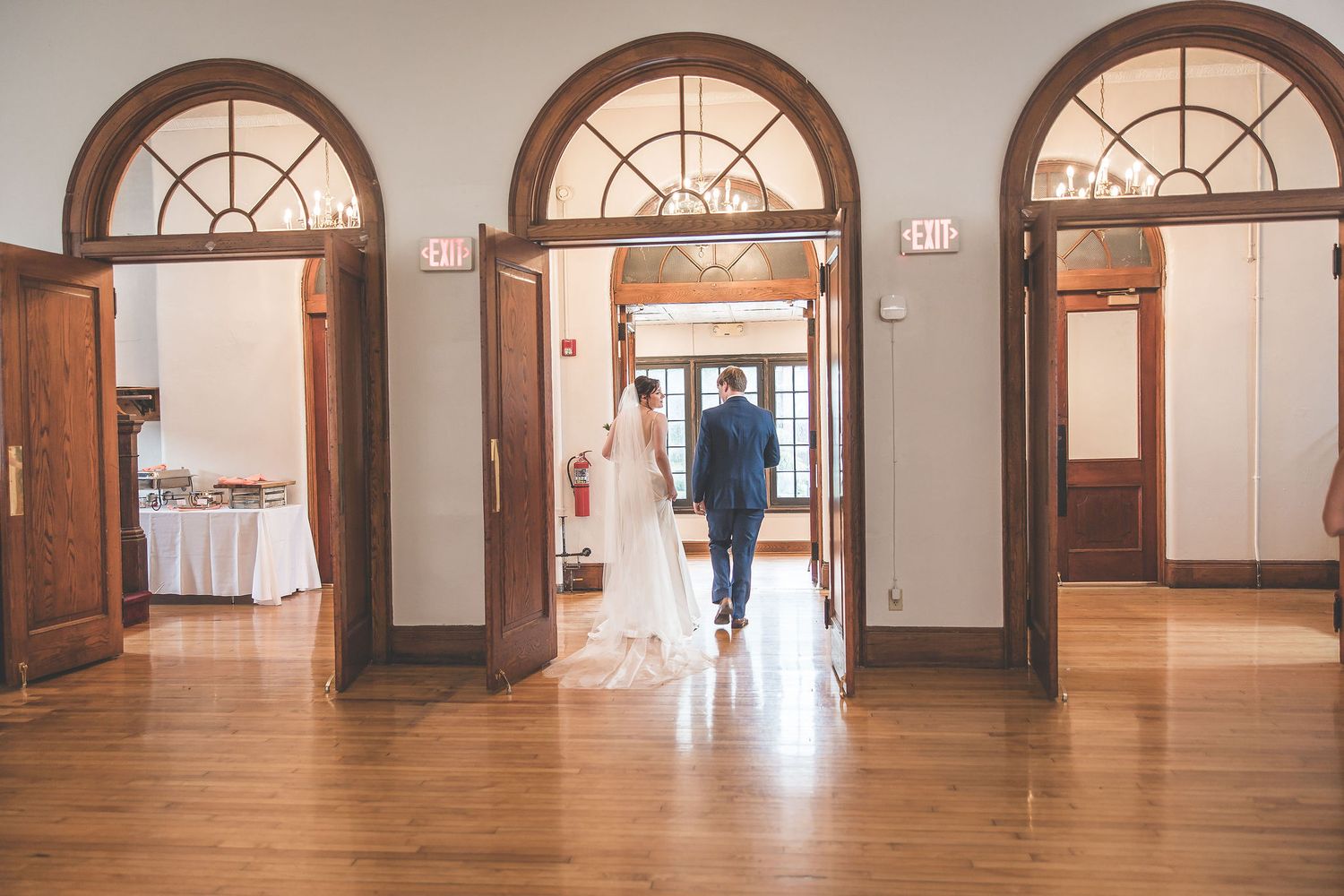 Architectural detail of wedding venue hallway featuring arched windows and hardwood floors.
