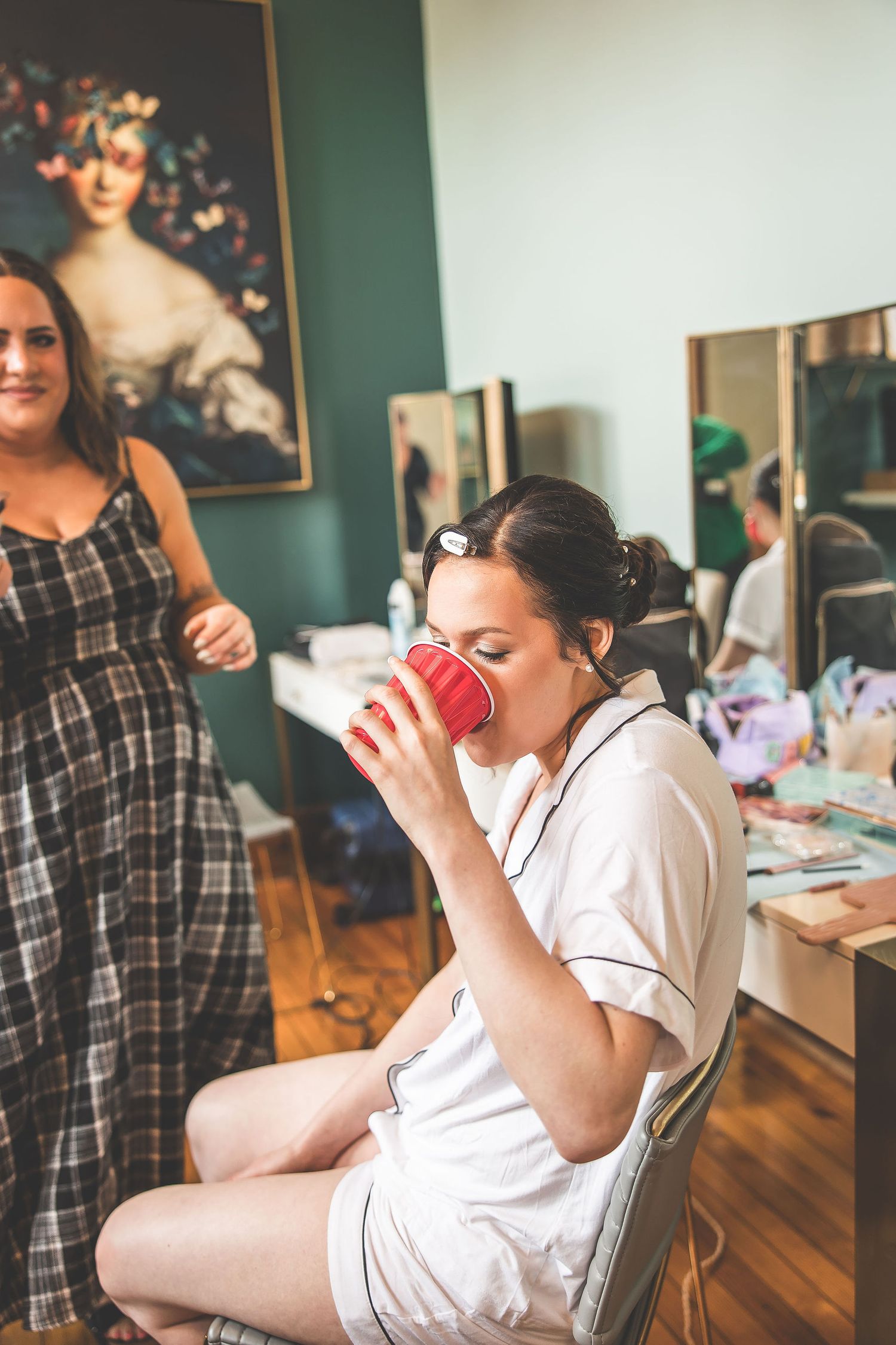 Person in white robe sipping from a red cup during wedding preparations.
