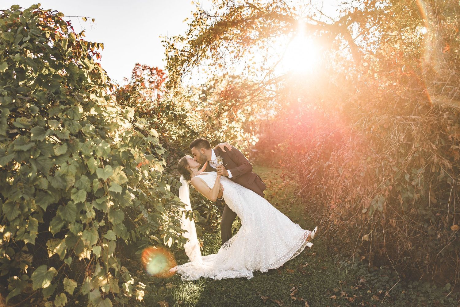 Dramatic sunset wedding photo with couple silhouetted against golden light through leaves.
