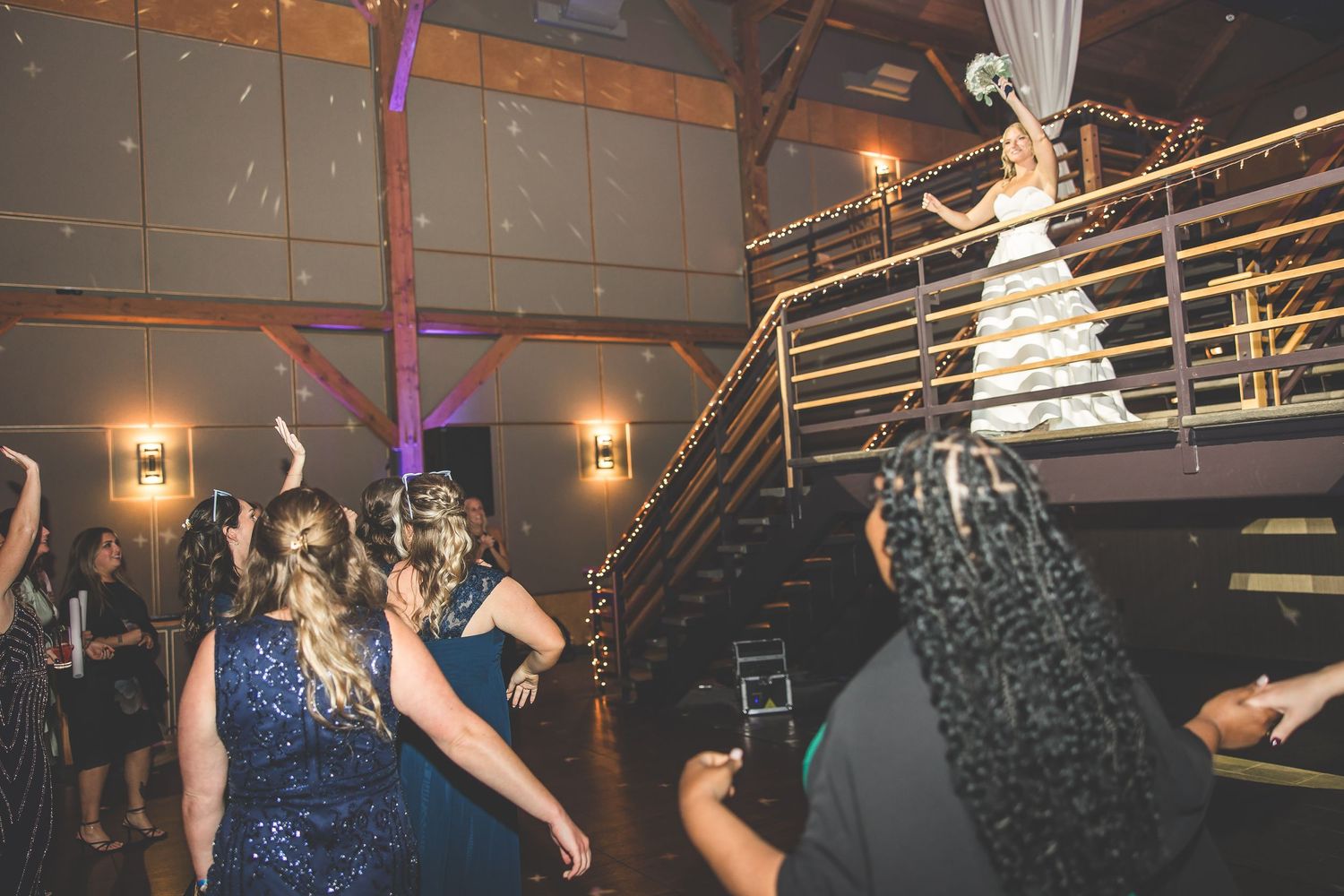 Wedding guests dancing and celebrating on dimly lit dance floor with purple lighting effects.