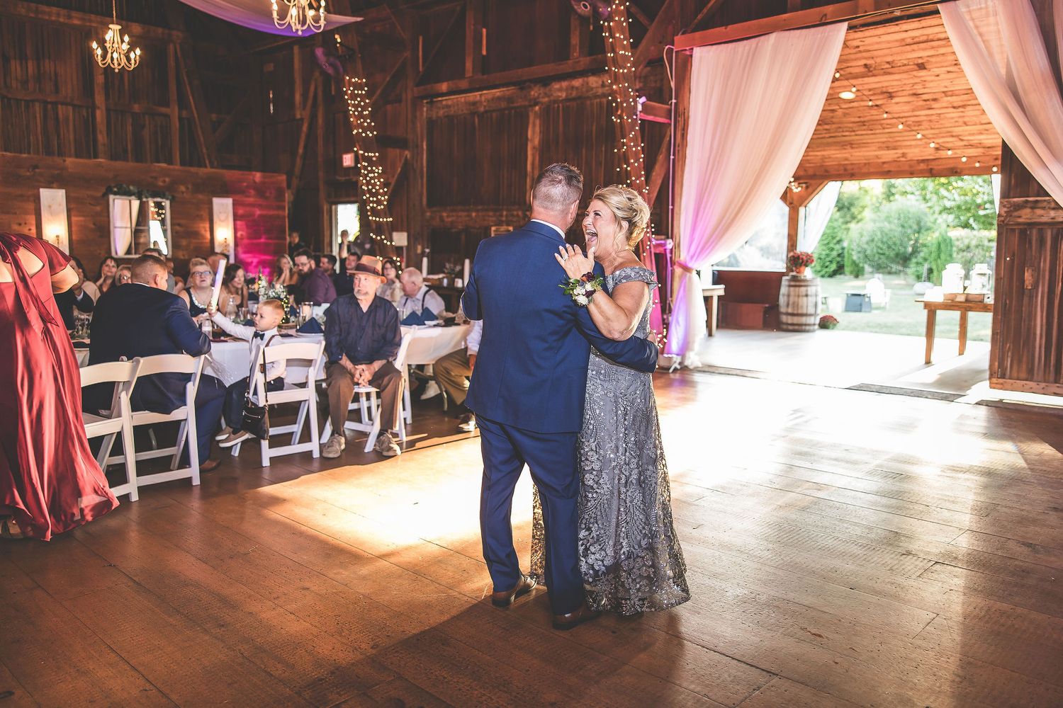 Wedding reception dance sequence in a rustic barn decorated with soft lighting and white drapes.