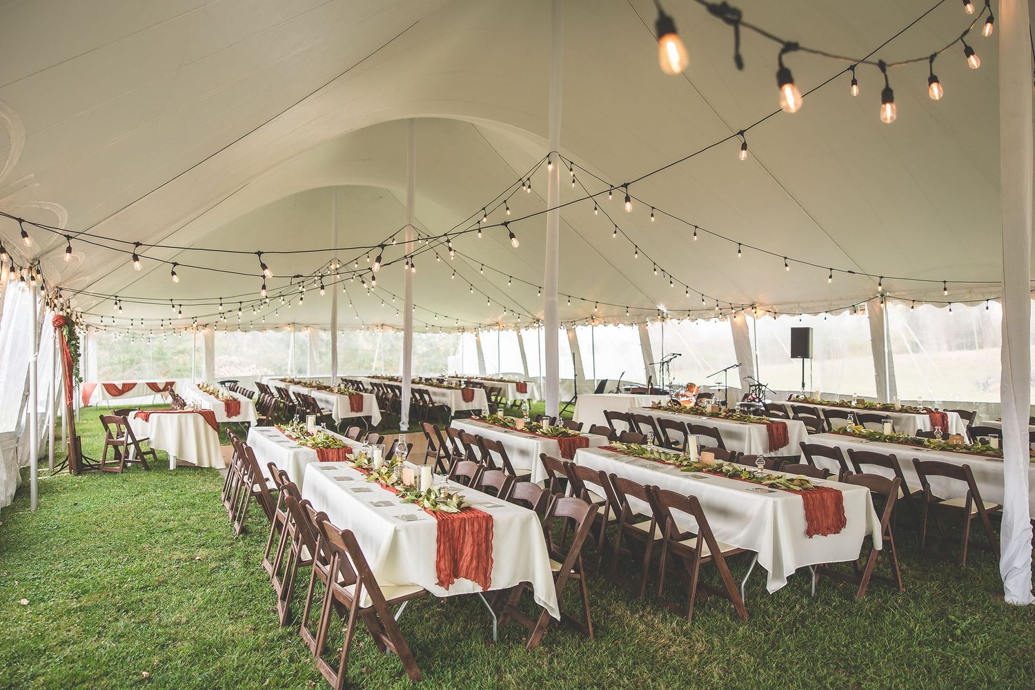 Large outdoor wedding reception tent with string lights and rows of decorated tables.