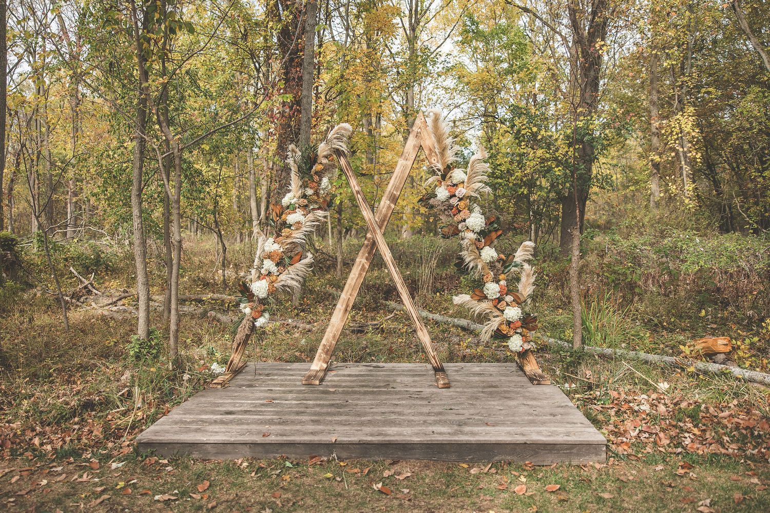 Outdoor wedding ceremony setup with wooden benches in a wooded autumn setting.
