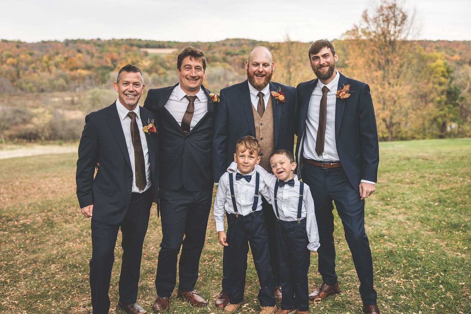 Groomsmen in navy suits and brown suspenders pose casually outdoors.