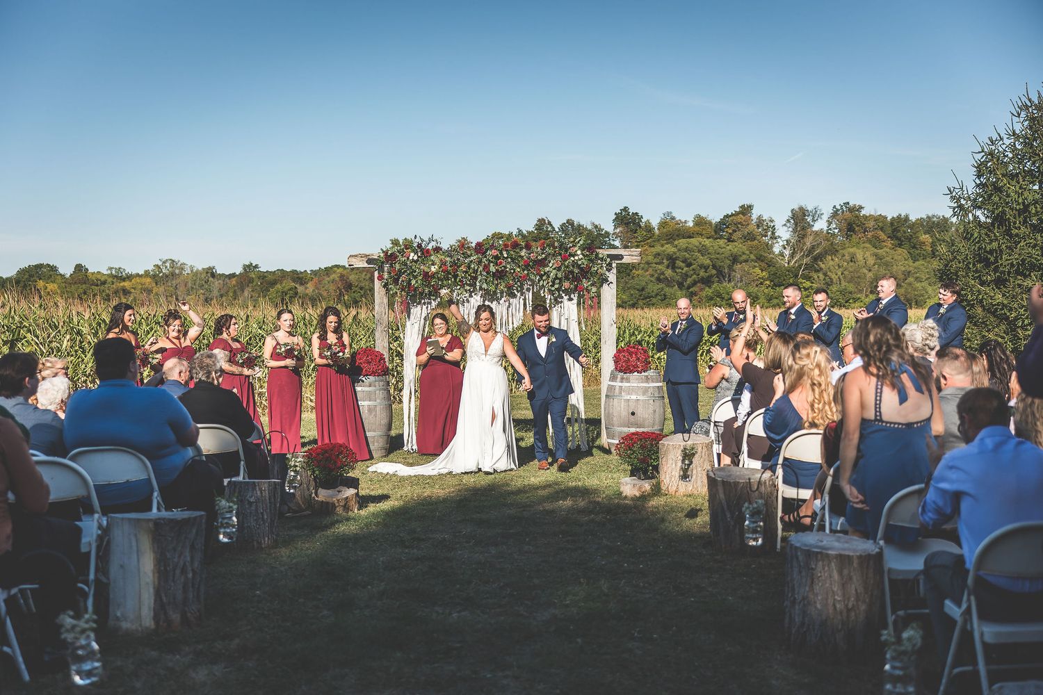 Outdoor wedding ceremony setup with rows of white chairs and guests seated under golden sunlight.