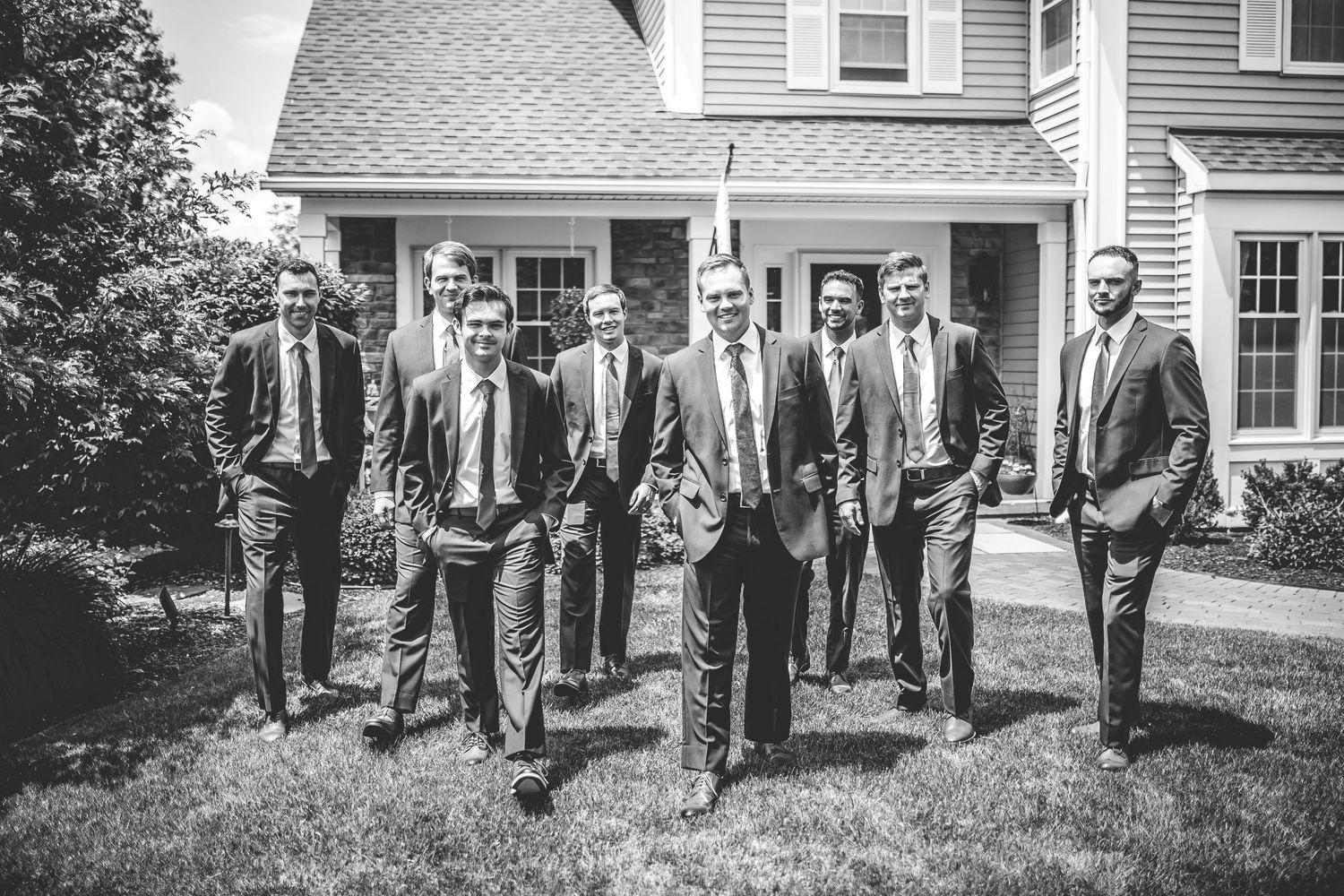 Black and white photo of groomsmen lined up outside a traditional house.