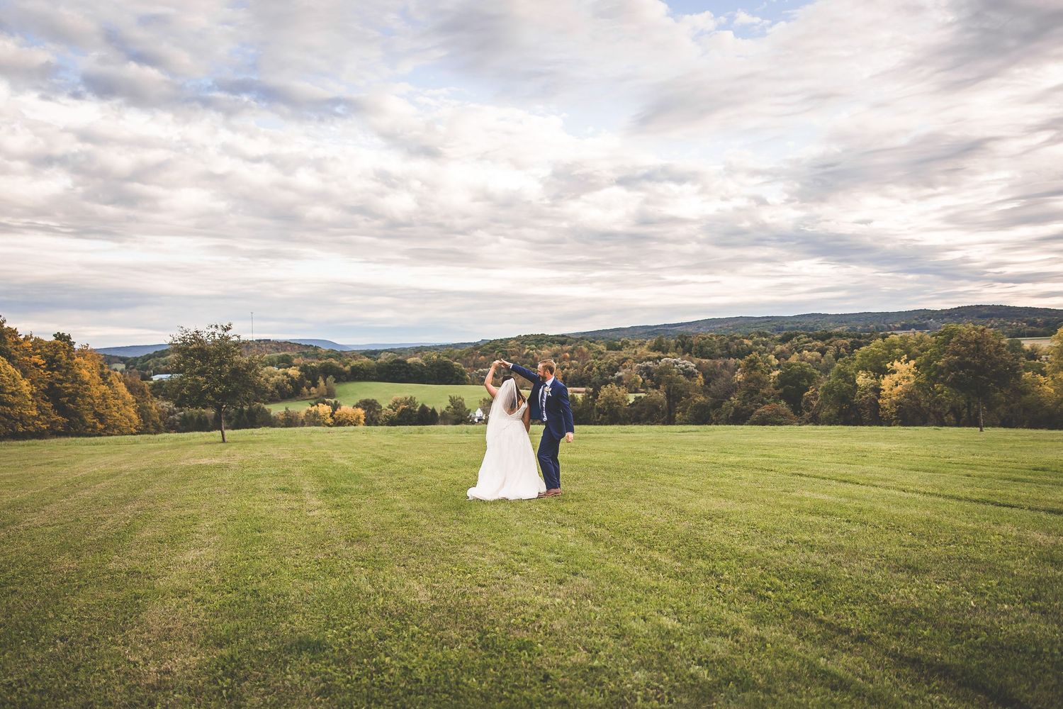 Panoramic view of a wedding venue with expansive green fields and distant hills under cloudy skies.