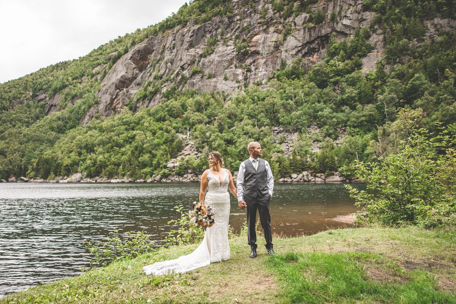 Scenic mountain cliffs and lake create dramatic backdrop for outdoor wedding photos.