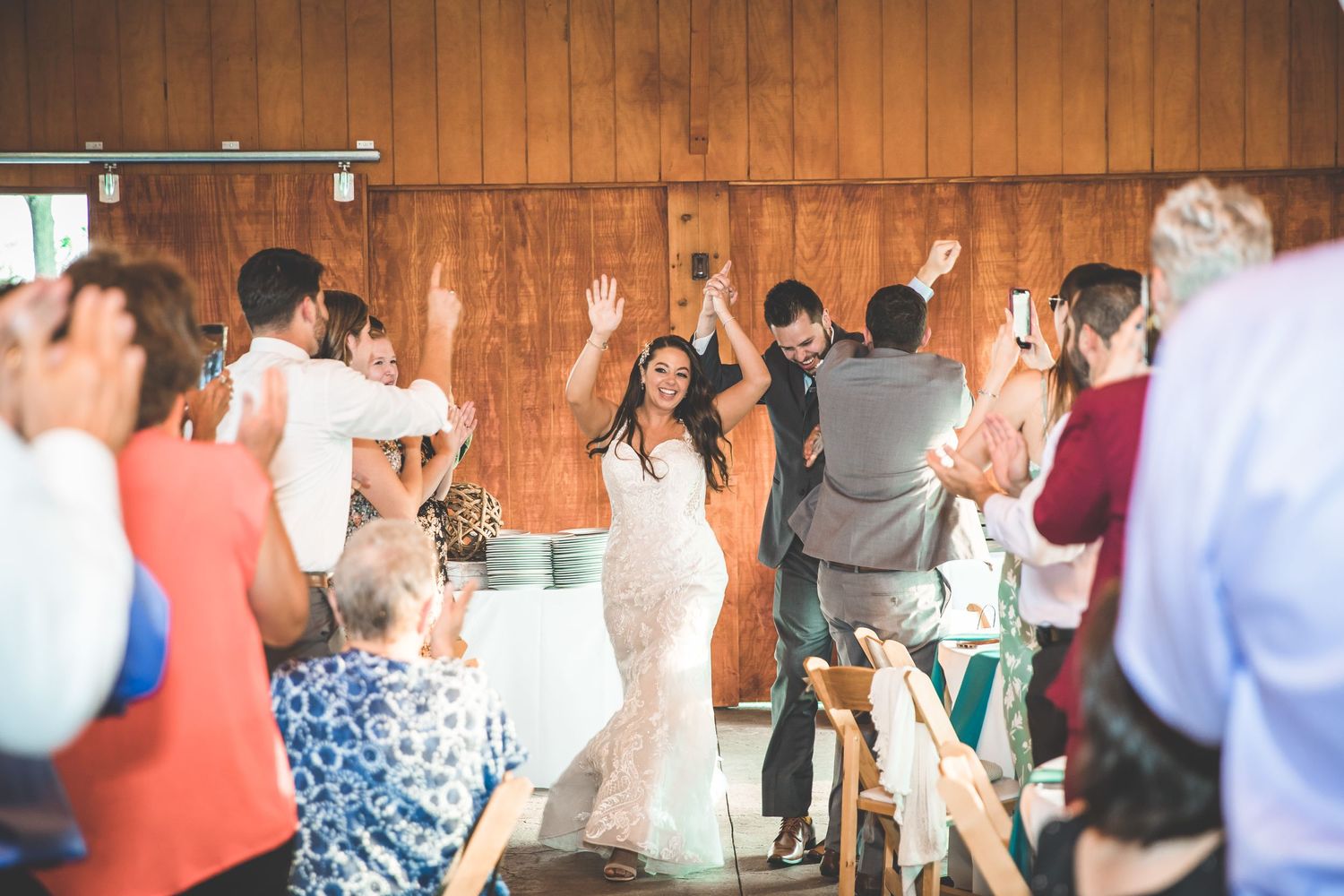 Wedding reception guests dancing and celebrating in a rustic wooden venue with string lights.