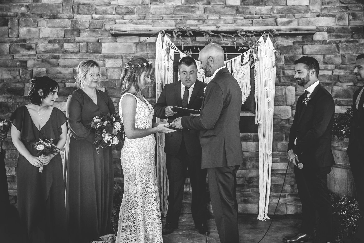 Wedding ceremony scene with attendees gathered in front of stone wall backdrop.