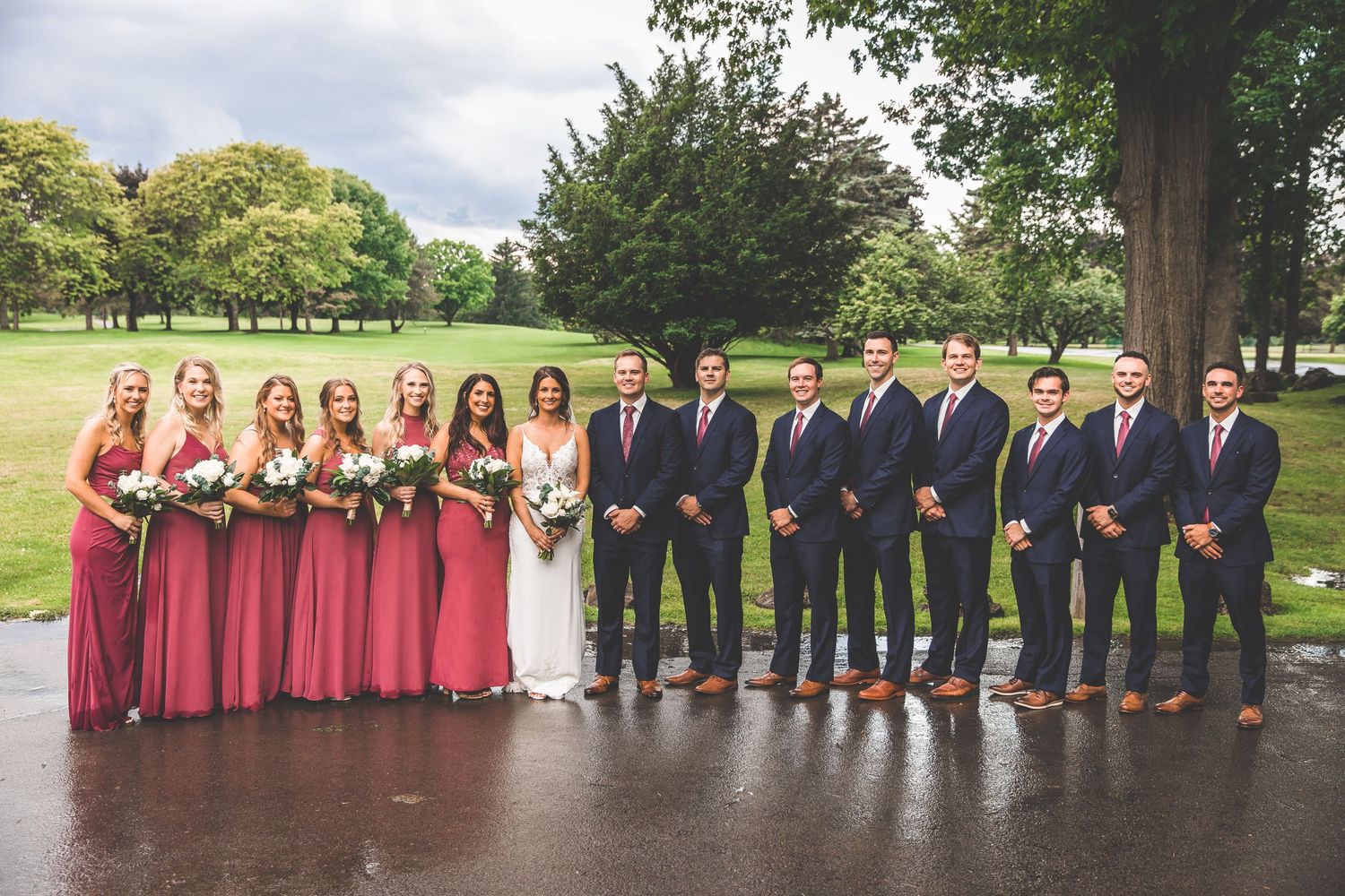 Full wedding party lineup with bridesmaids in burgundy and groomsmen in navy suits.