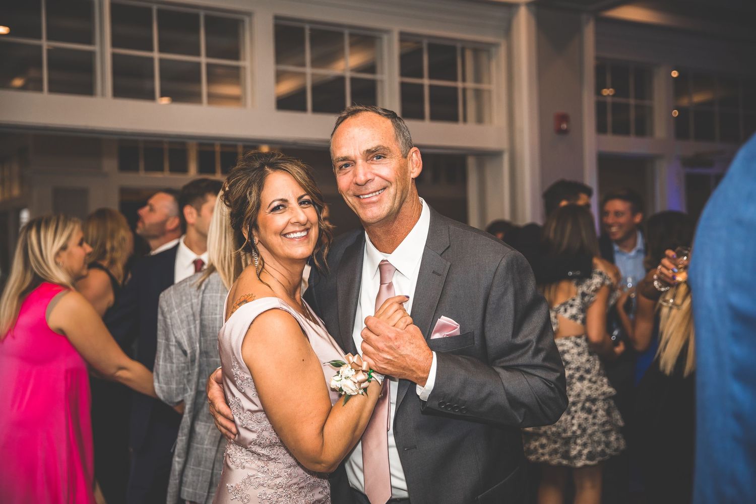 Wedding guests dancing and celebrating on a lively dance floor at an indoor reception venue.